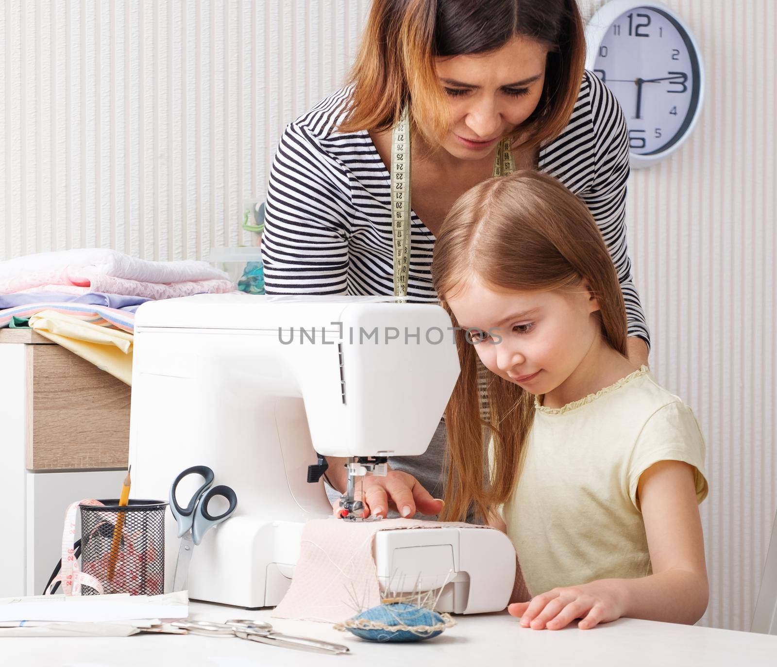 Attractive woman showing child pupil how to easy work with sewing machine at home