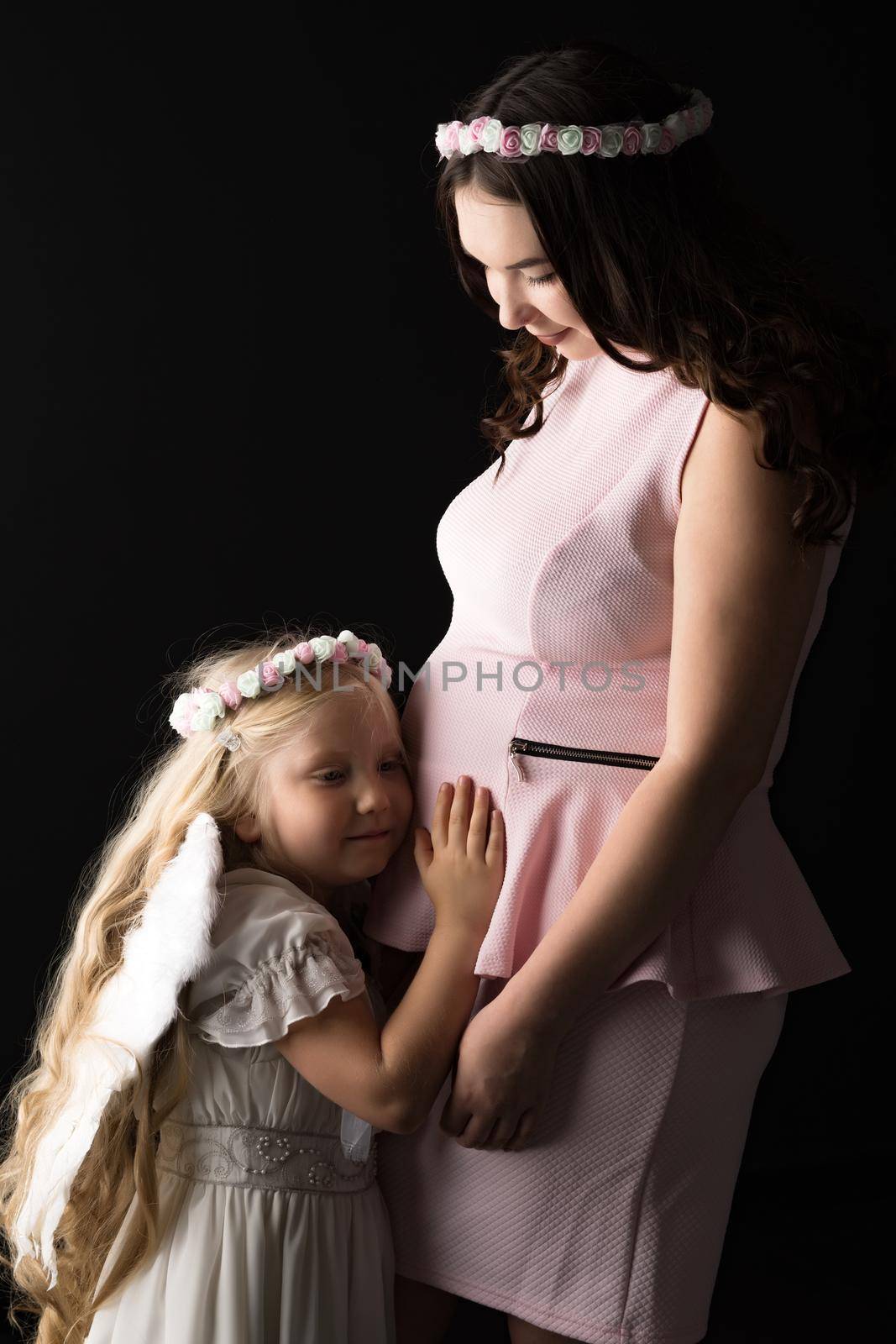 The girl in the image of an angel hugs the tummy of her eldest p by kolesnikov_studio