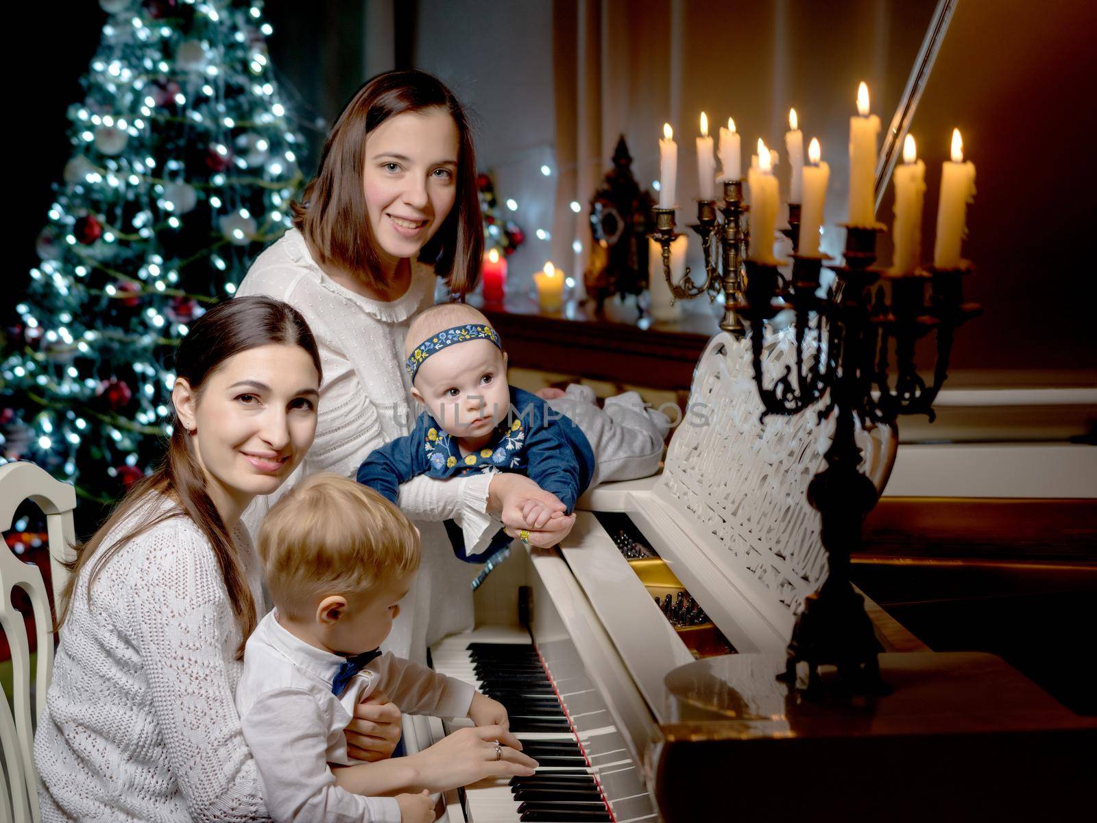 Young mothers with their young children in a dark room by candlelight, near a large white grand piano. The concept of holidays and happy childhood.