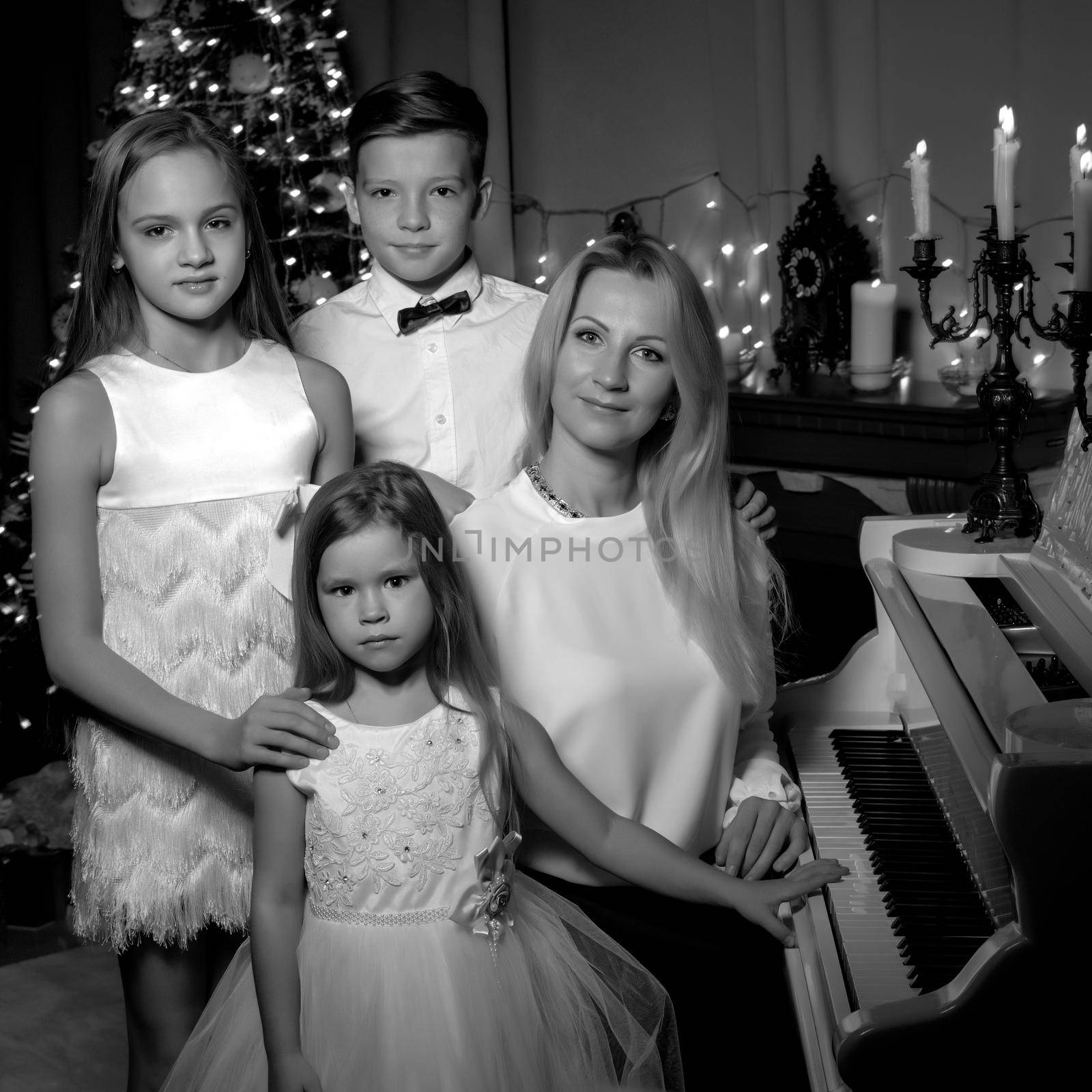 A happy mother with young children on Christmas Eve in a dark room with candles and a fireplace, near a large white grand piano. The concept of a family holiday.