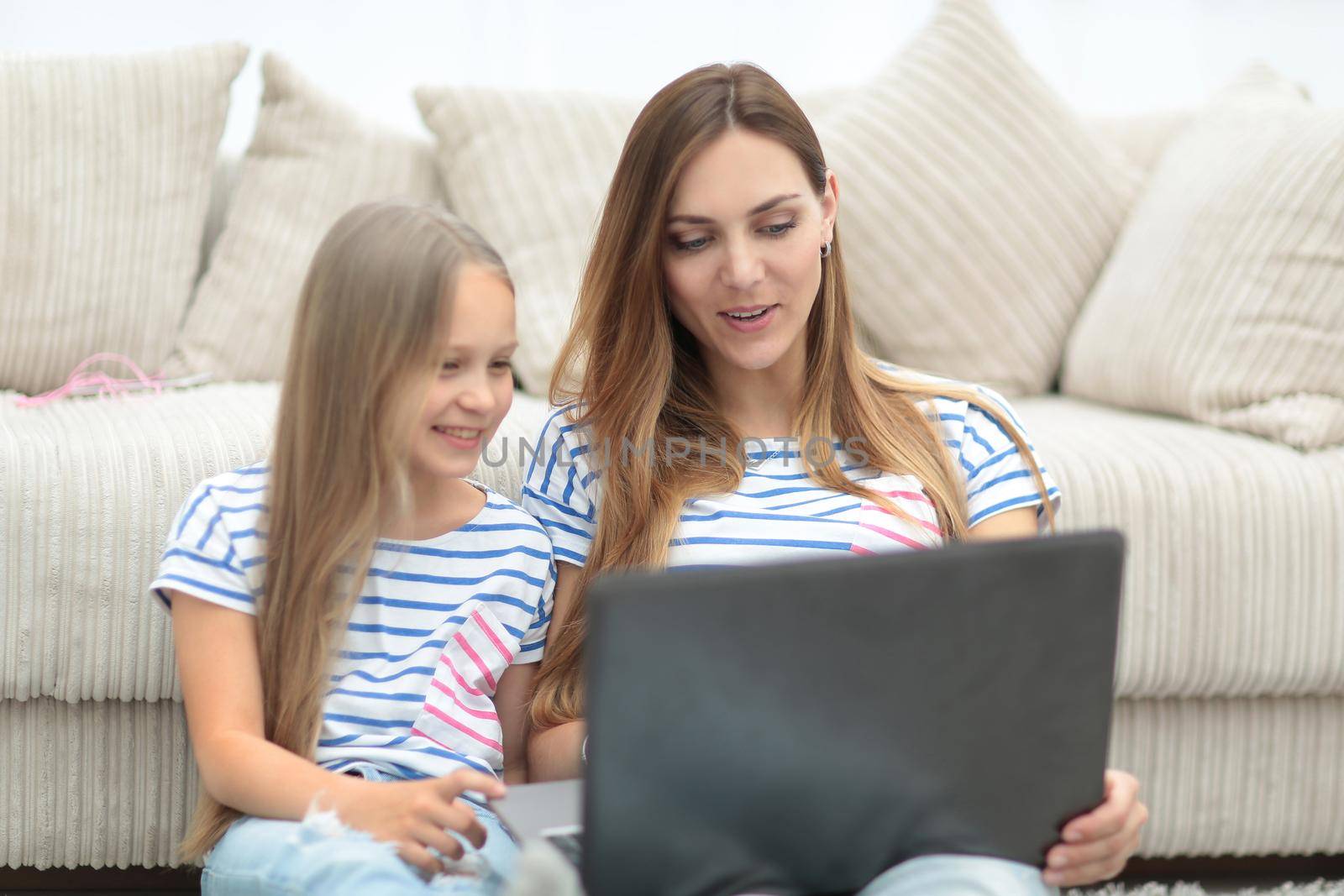 mom and daughter lying sitting in the living room and using a laptop by asdf