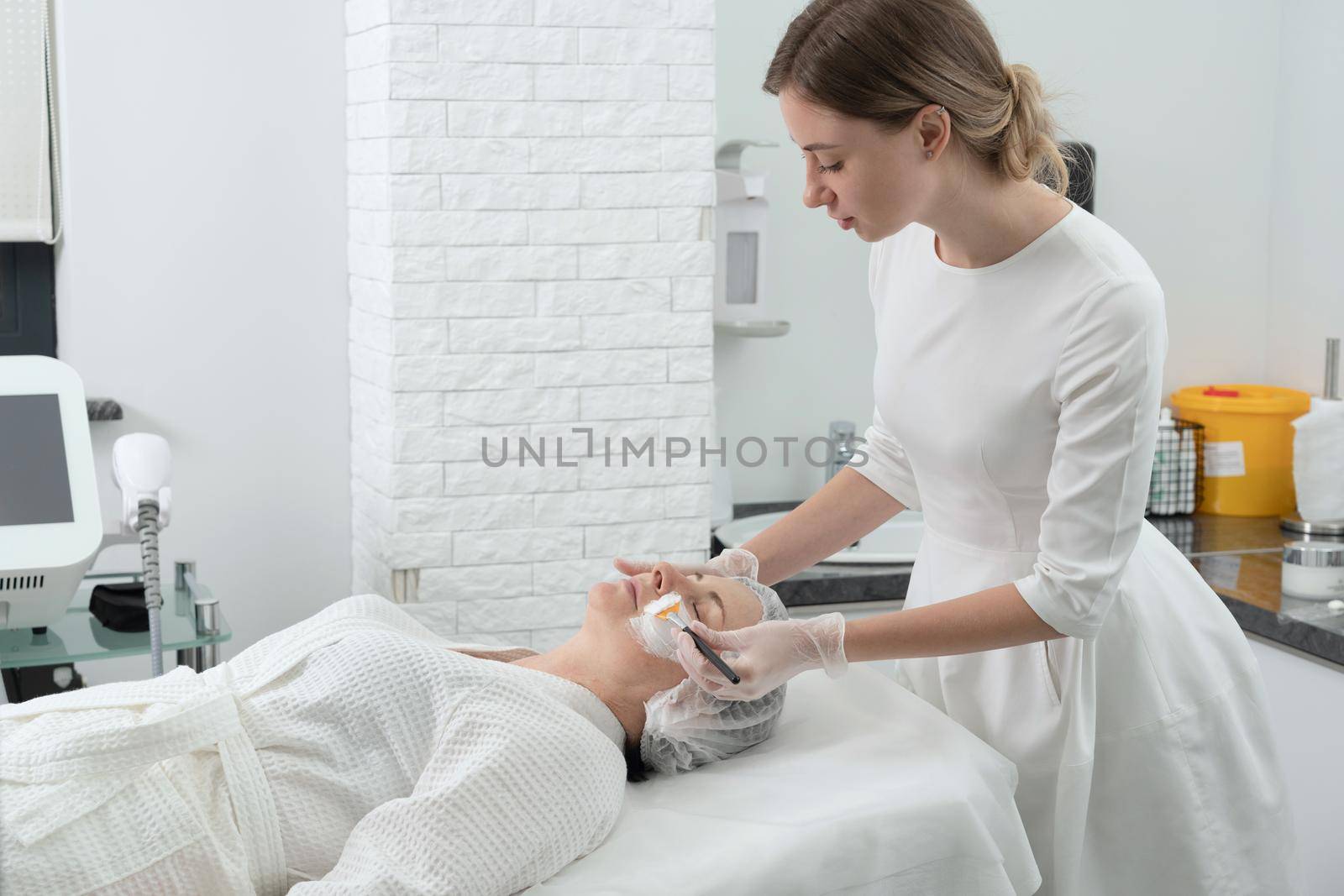 Mature woman receiving wwhte facial mask in spa beauty salon. Concept of skin care for older people by Mariakray