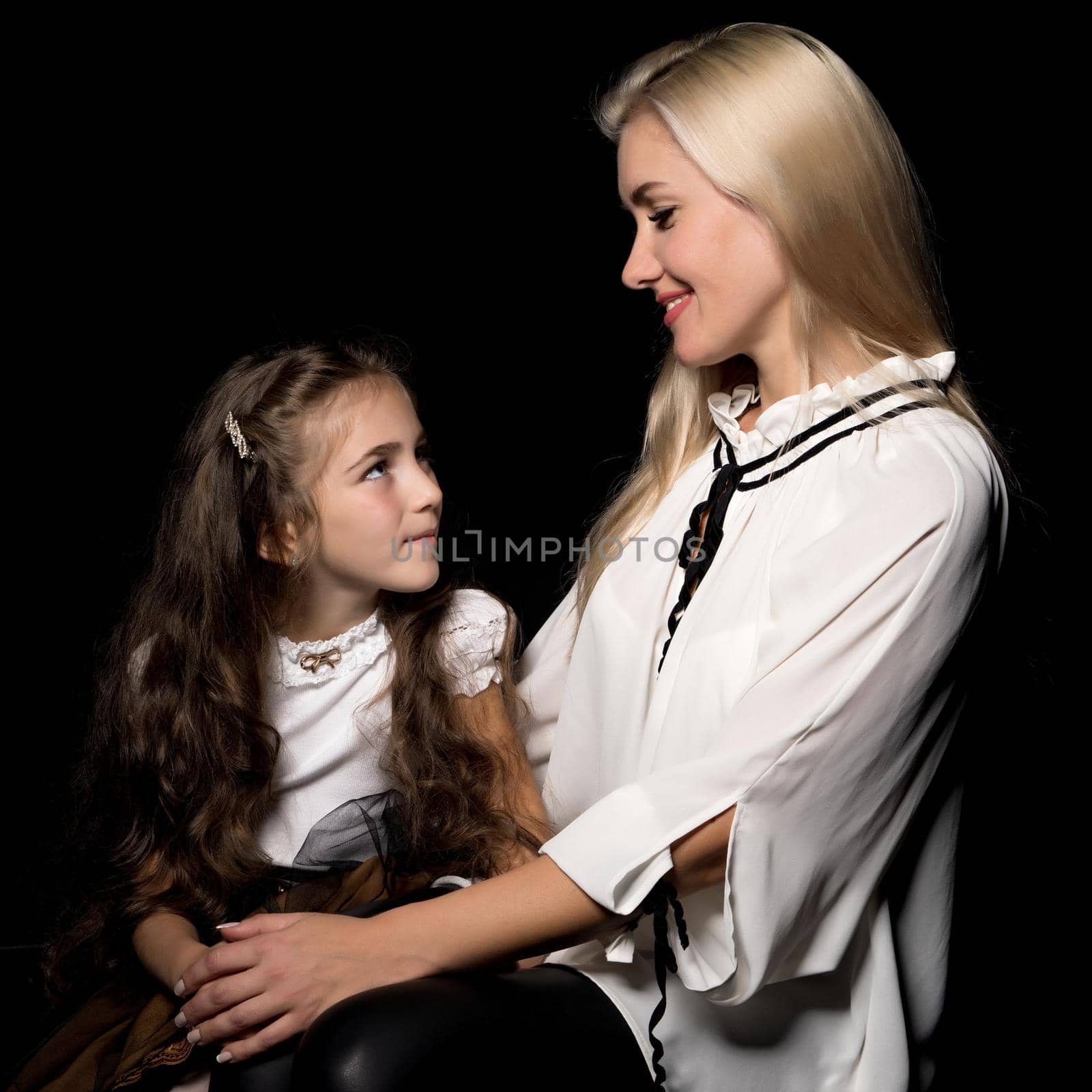 Beautiful young mother with a little daughter in her arms, studio on a black background. The concept of a happy childhood, advertising.
