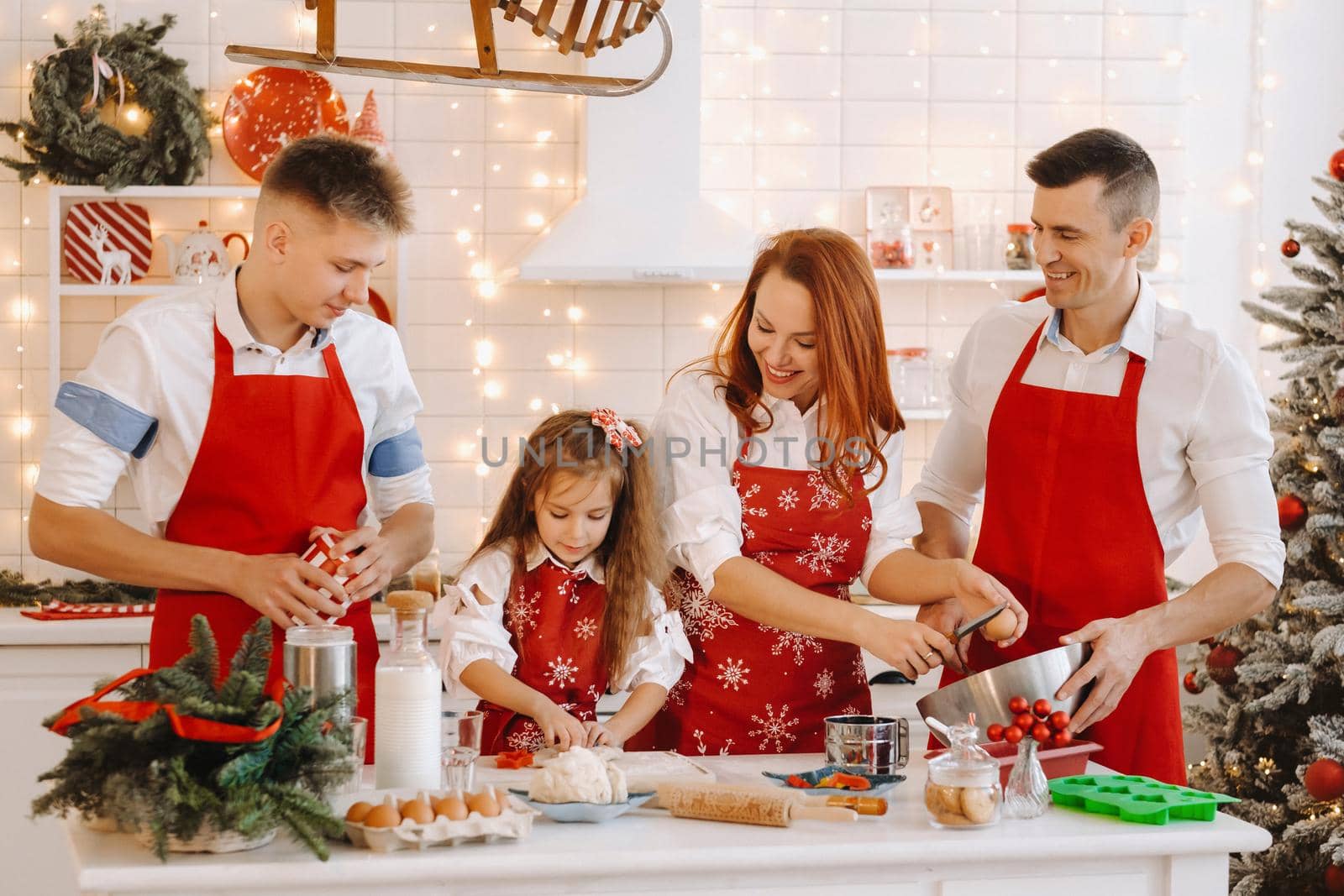 A happy family is standing in the Christmas kitchen and preparing dough for making cookies.