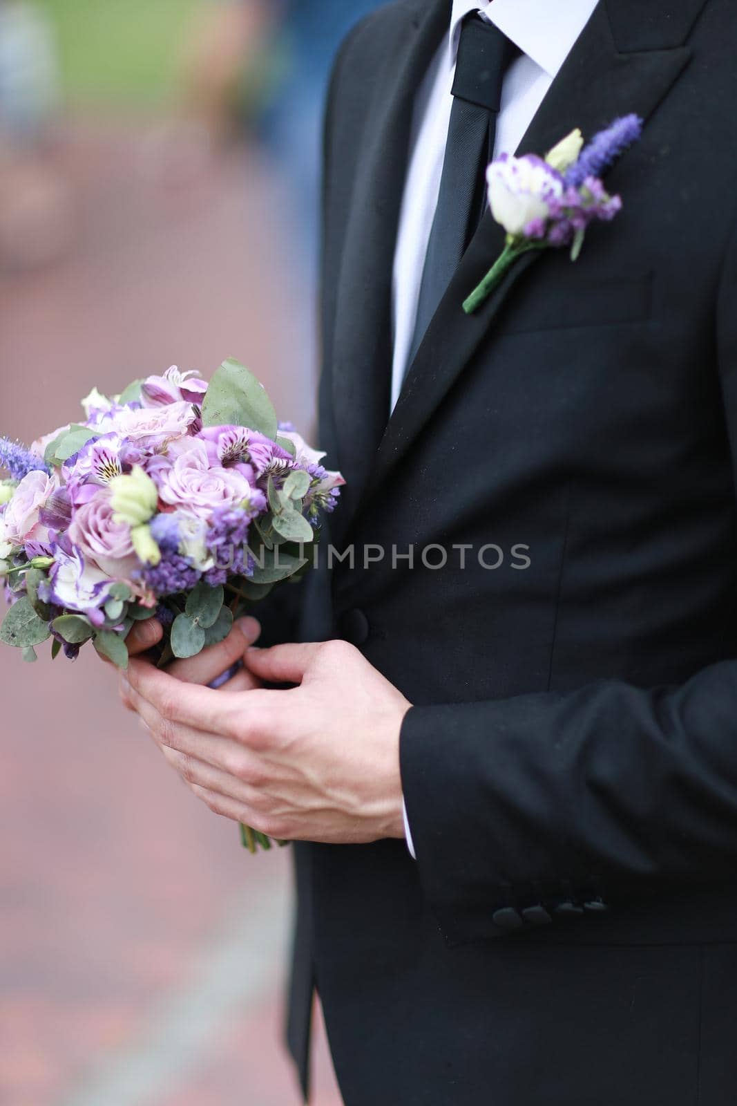 Caucasian groom wearing black suit and tie keeping bouquet of flowers. by sisterspro