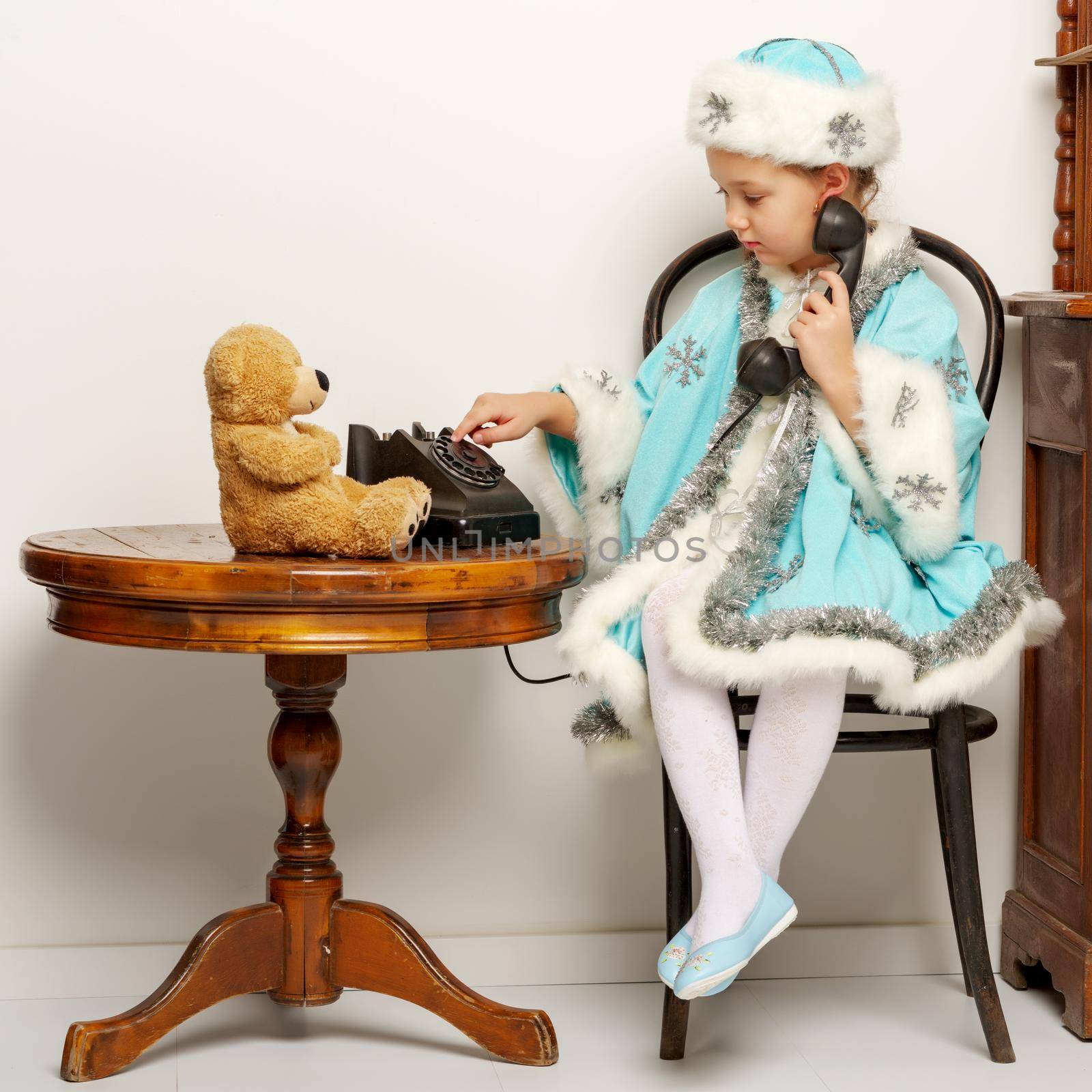 Cute little girl in a snow maiden costume talking on the old phone. The concept of family holidays.