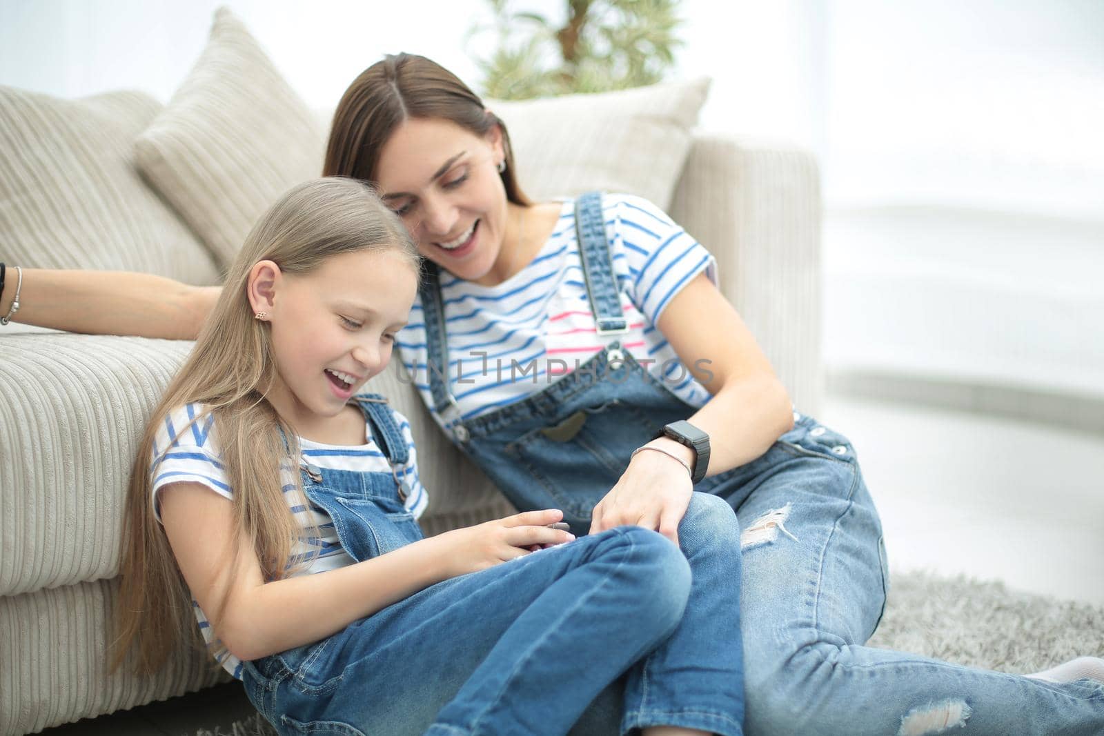 Mother with a little daughter using a smartphone sitting in the new living room.people and technology