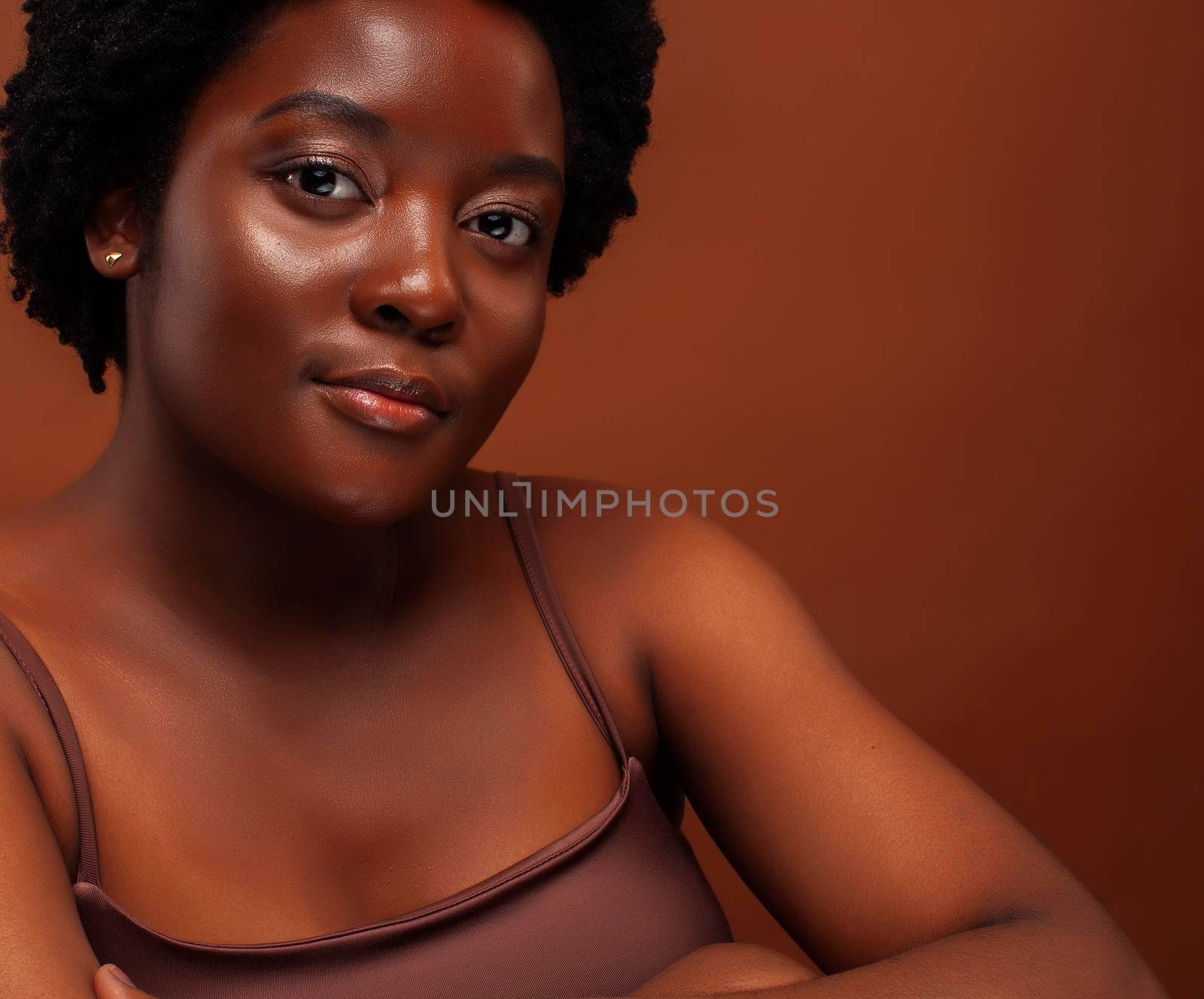 pretty young african american woman with curly hair posing cheerful gesturing on brown background, lifestyle people concept close up