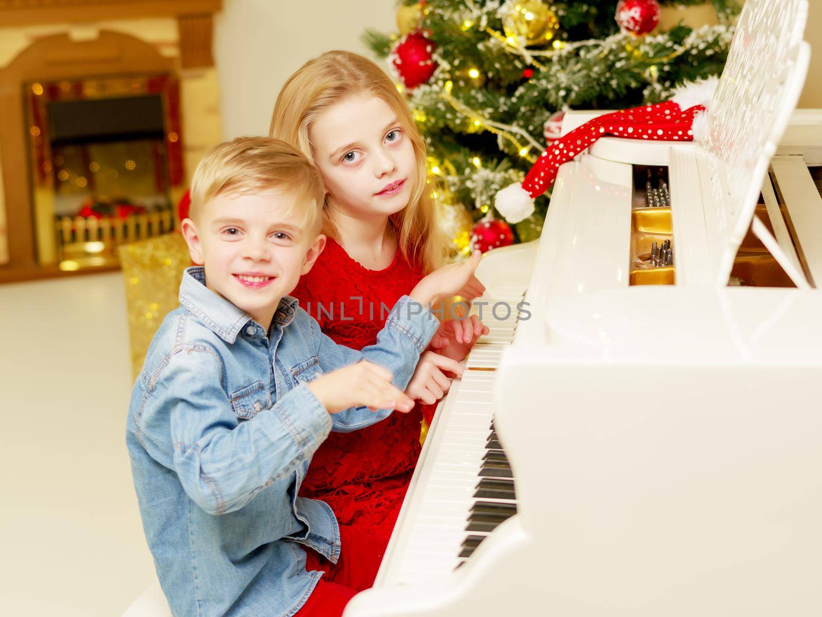 Brother and sister play the piano on Christmas Eve at the Christmas tree. The concept of a holiday, a happy childhood.