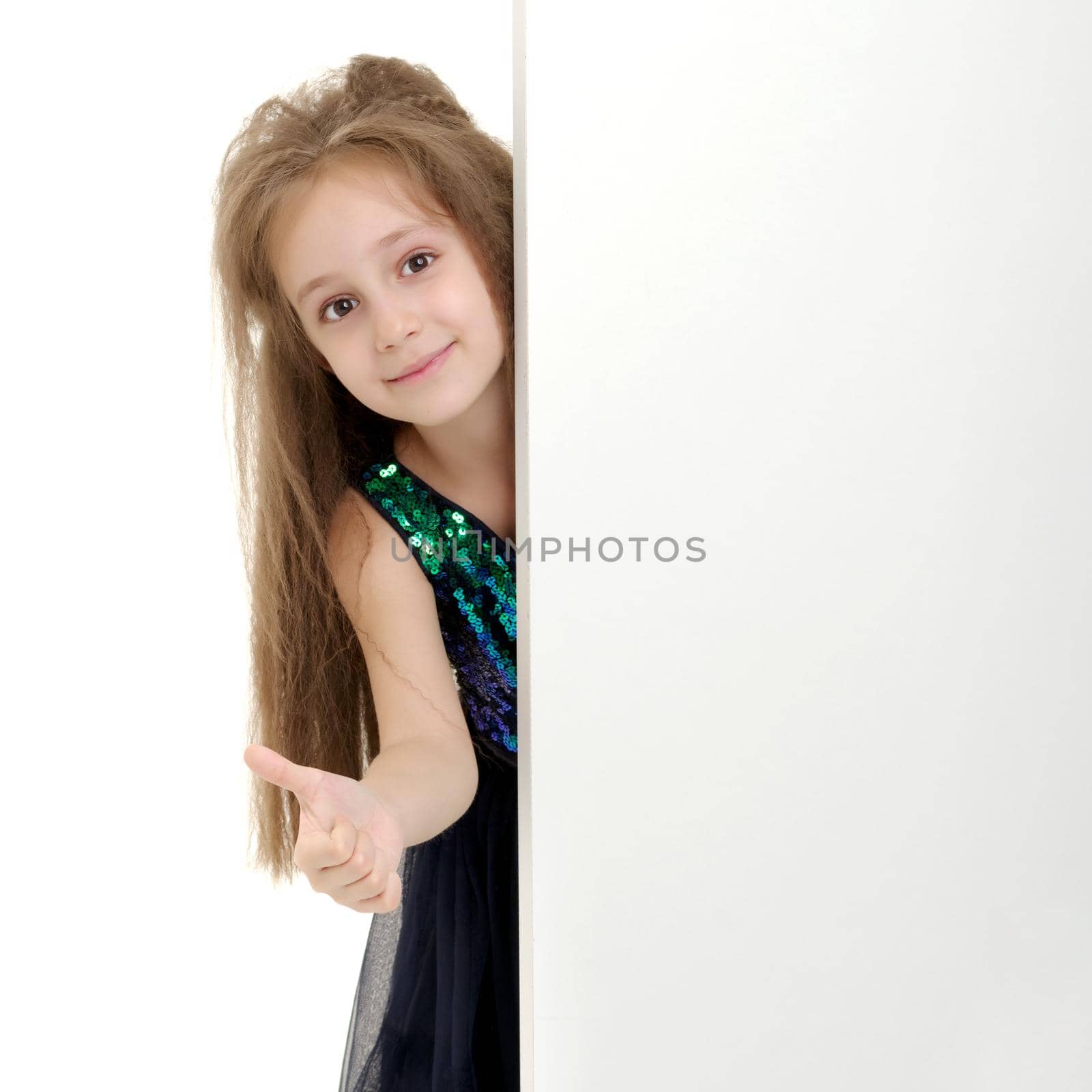 A nice little girl is looking because of an empty banner in which you can insert any text. The concept of a happy childhood, advertising, selling goods. Isolated on white background.