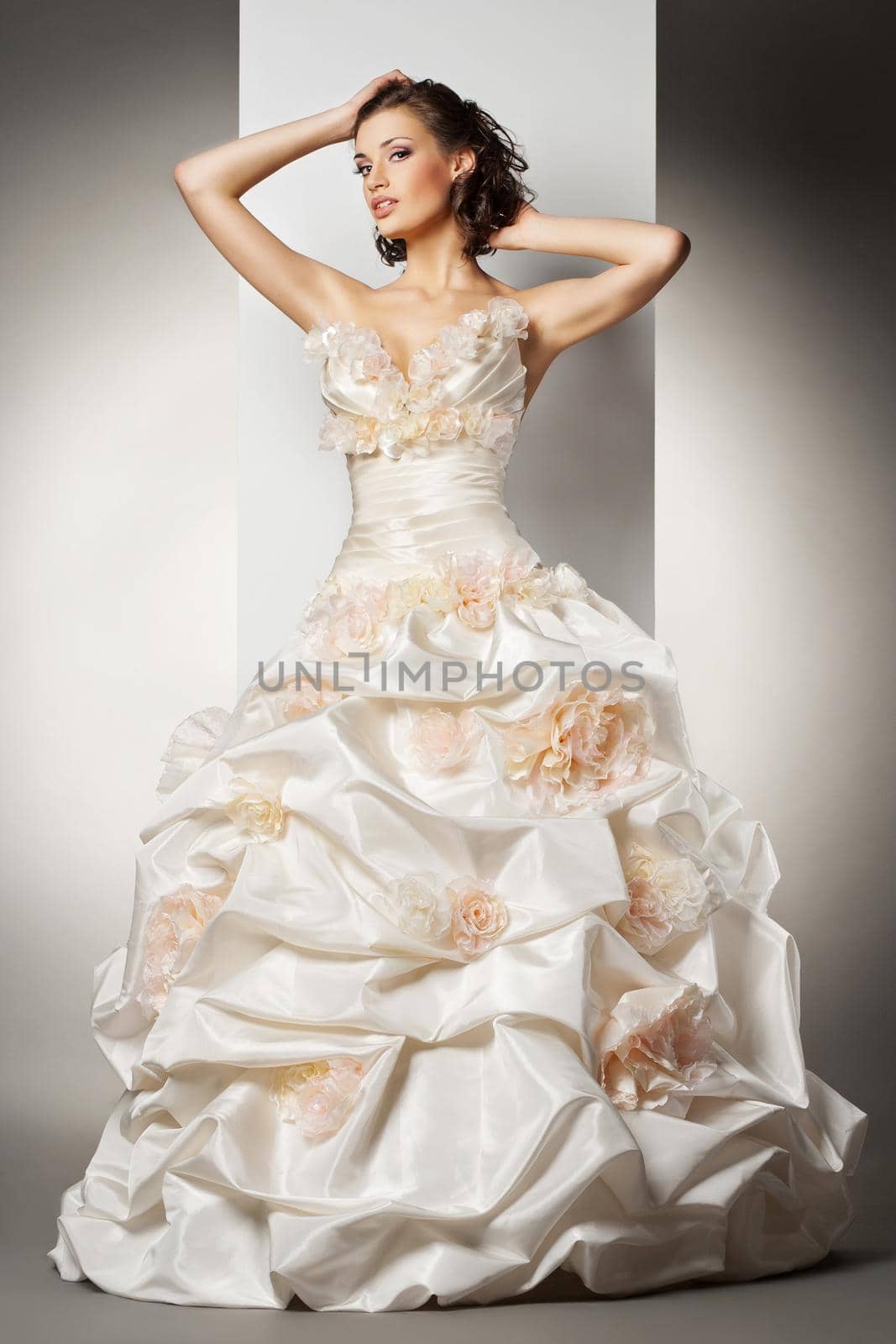 The beautiful young woman posing in a wedding dress over grey backround
