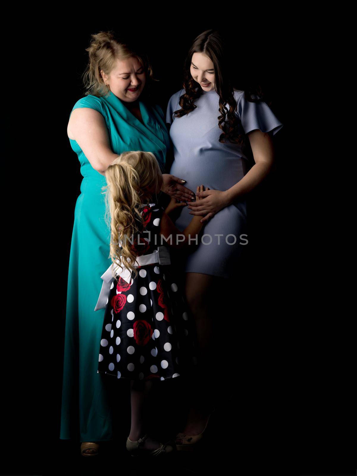 Young pregnant girl with her mother and younger sister on a black background.