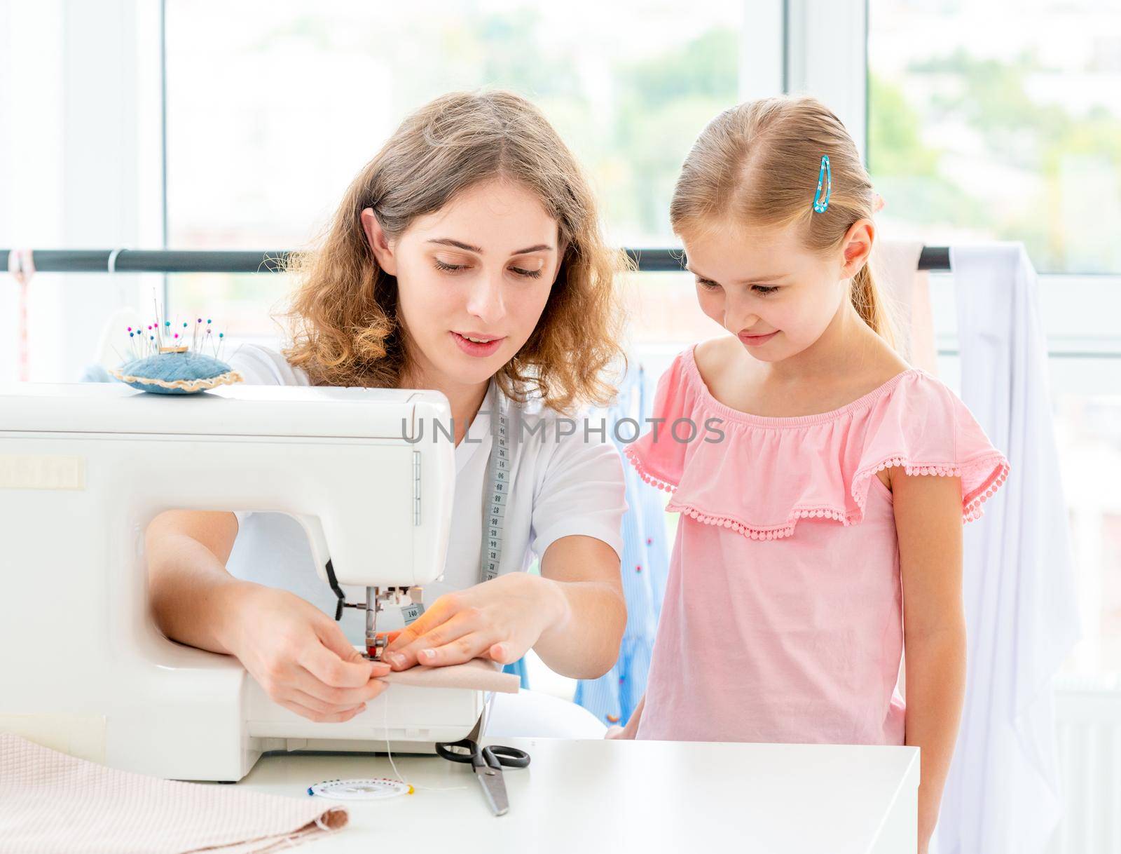 Little girl is taught to sew by teacher at class