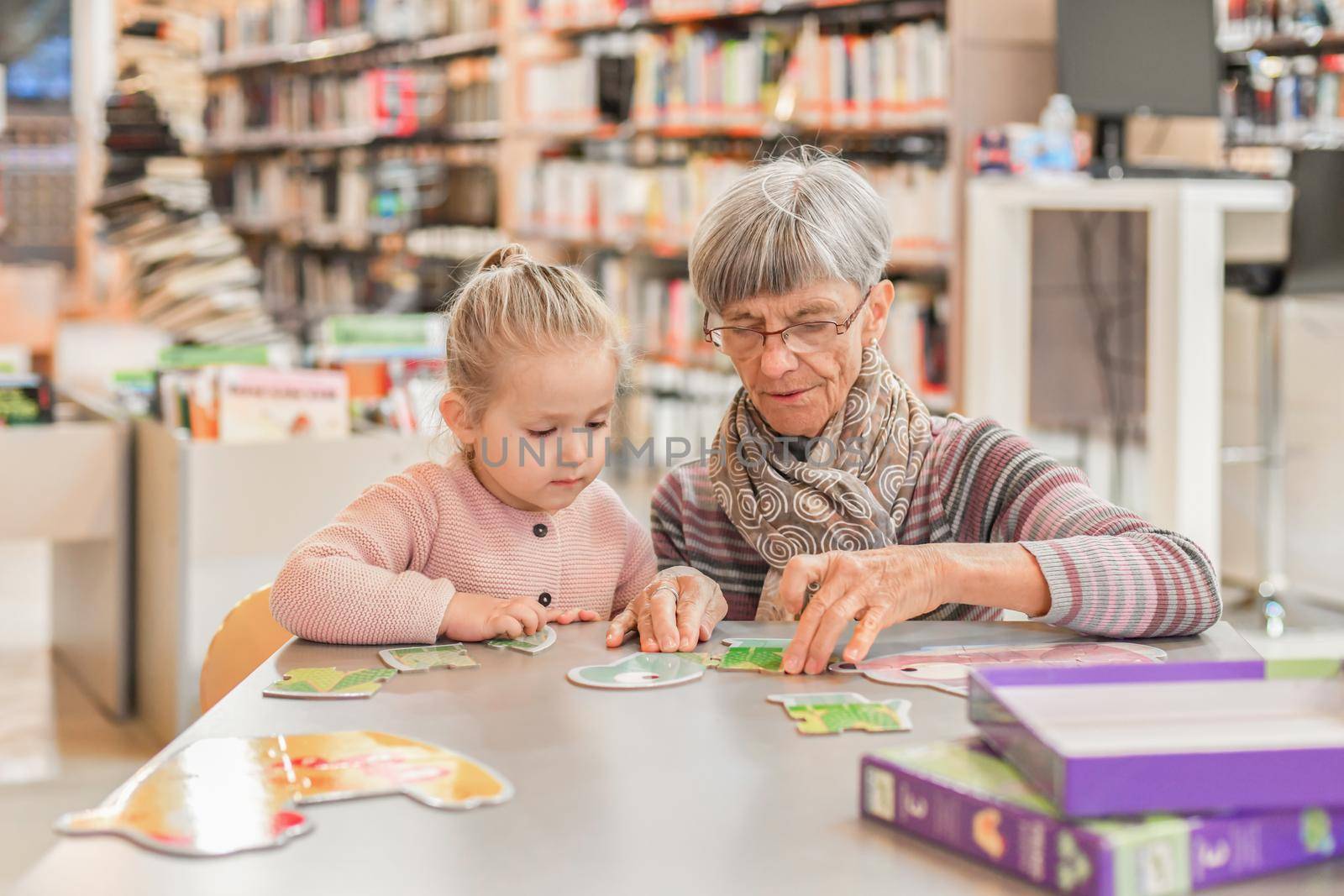 Granddaughter and grandmother put together a puzzle in the city library by Godi