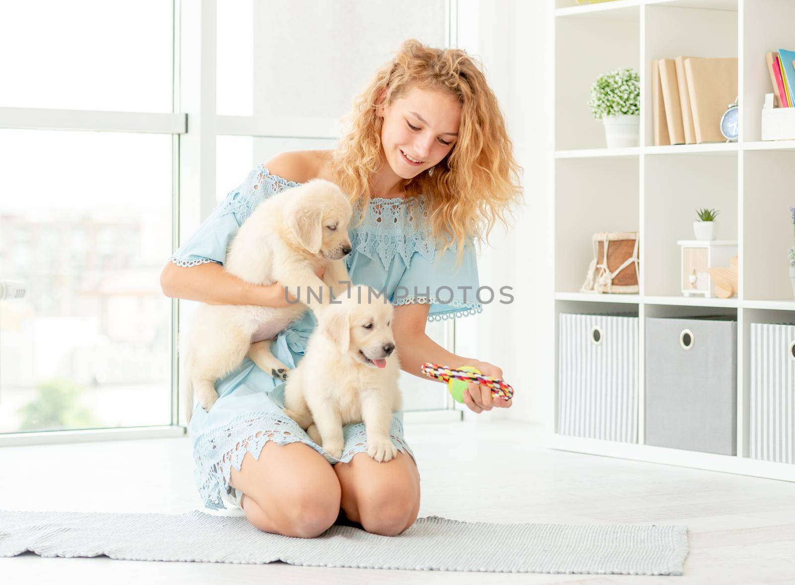 Happy girl teaching puppies to sit at home
