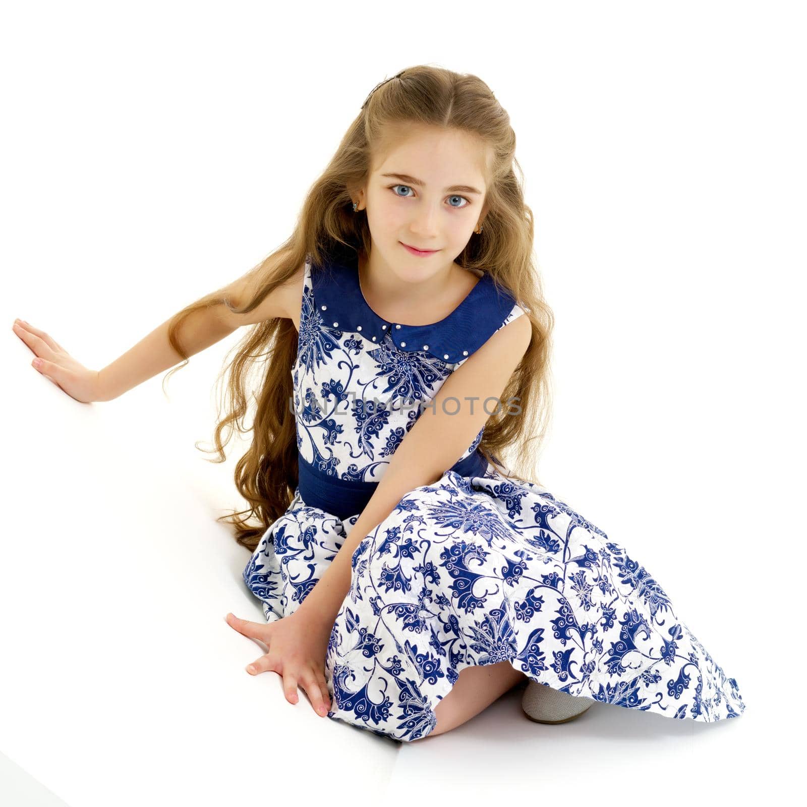 Beautiful little girl is sitting on the floor in the studio. The concept of a happy childhood, beauty and fashion. Isolated on white background.