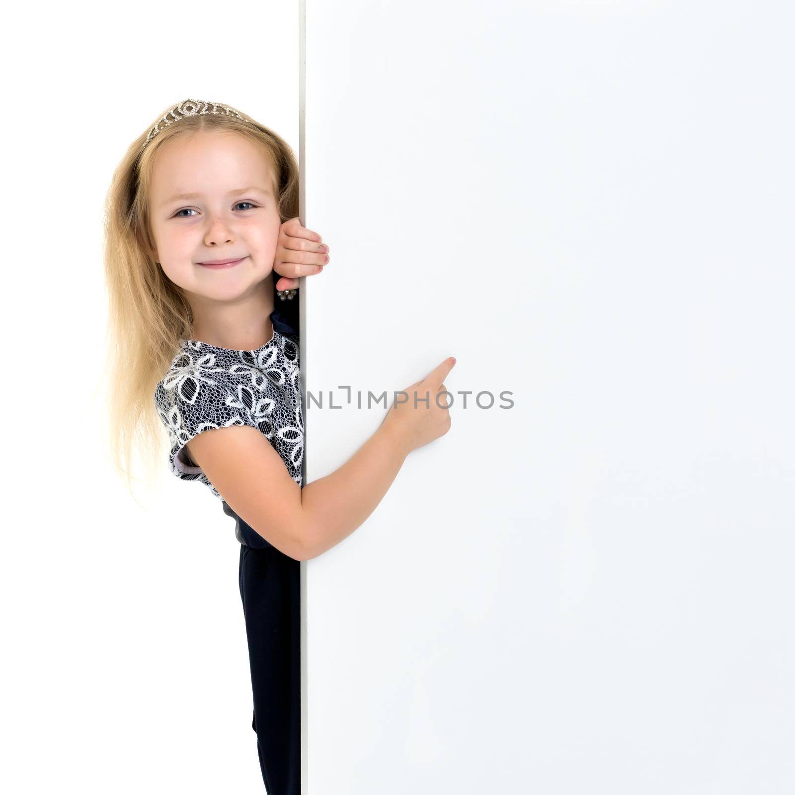 A nice little girl points a finger at a large white banner on which you can write any advertisement. The concept of promotion of goods, happy childhood. Isolated on white background.