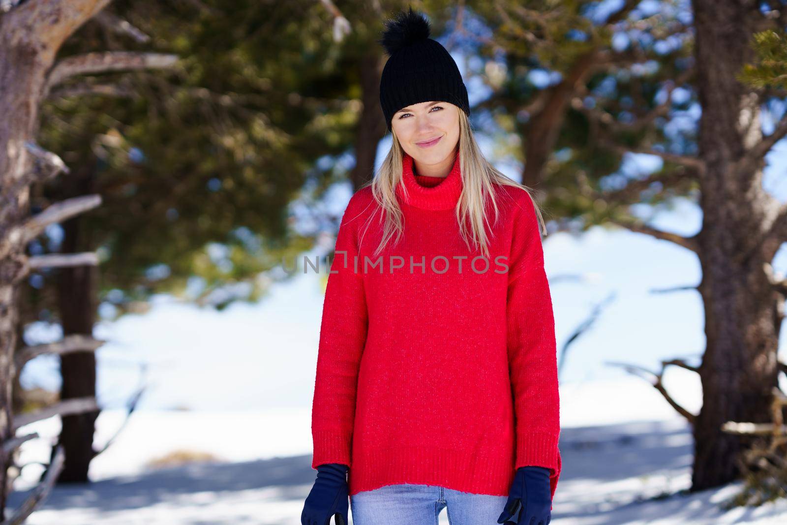 Young blonde woman in a snowy forest in the mountains, in Sierra Nevada, Granada, Spain. Female wearing winter clothes.