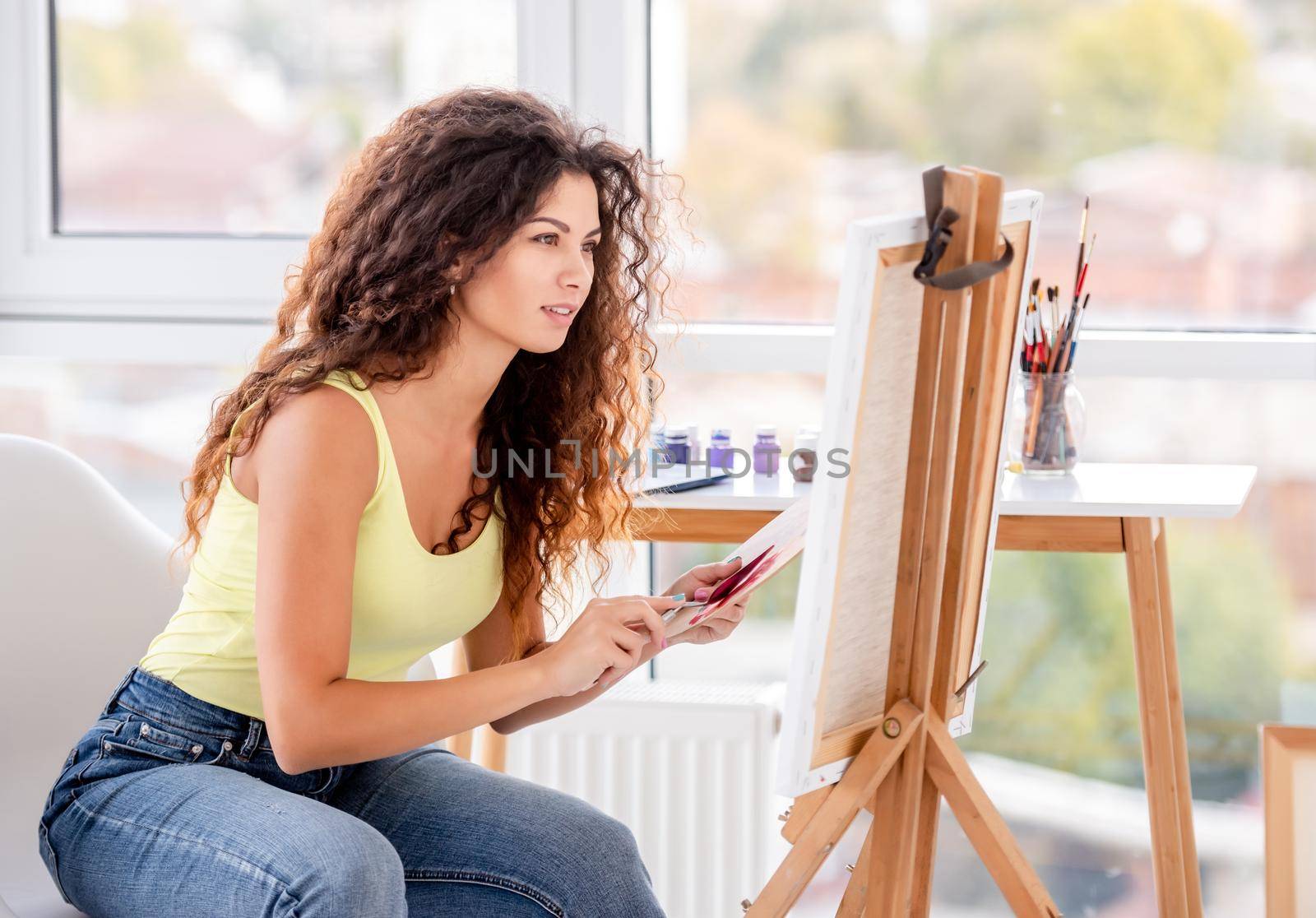 Smiling artist painting on easel in workshop