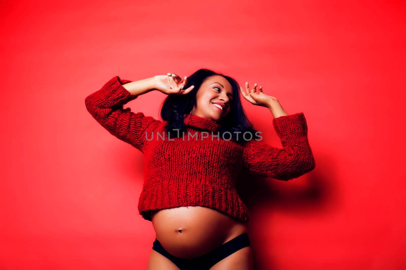 close up portrait of pregnant woman with big belly, hands hold, red sweater on background, choise of gender, lifestyle people concept