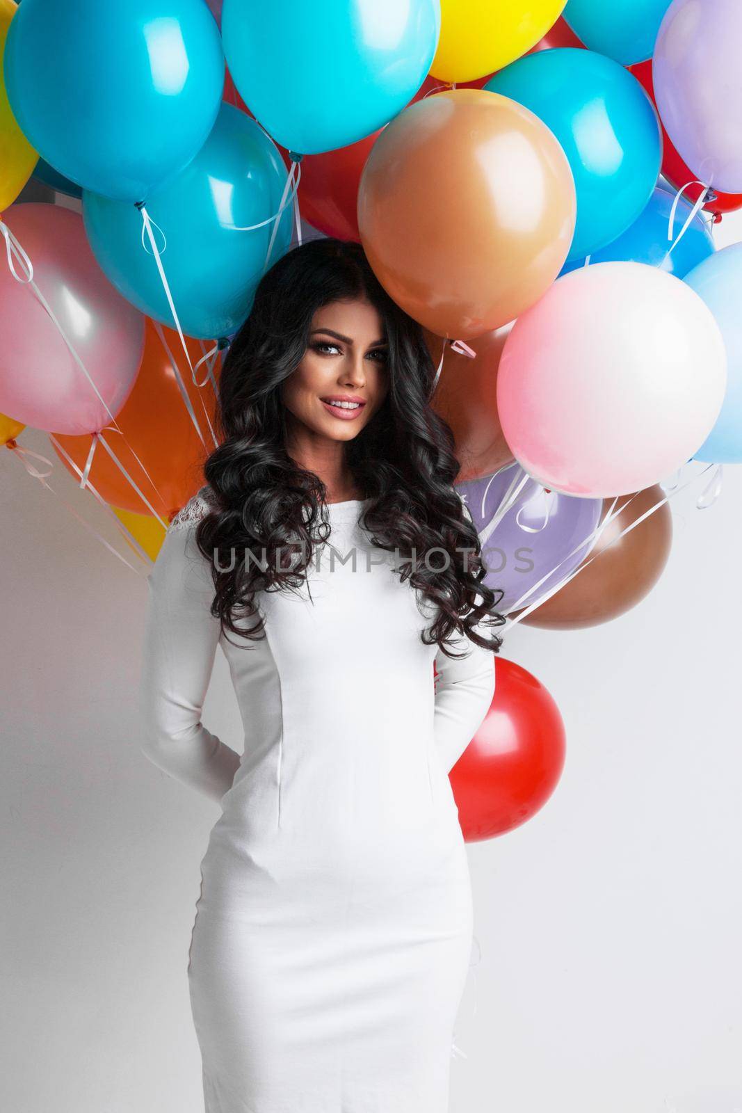 Young pretty woman in white dress with many color balloons on white background