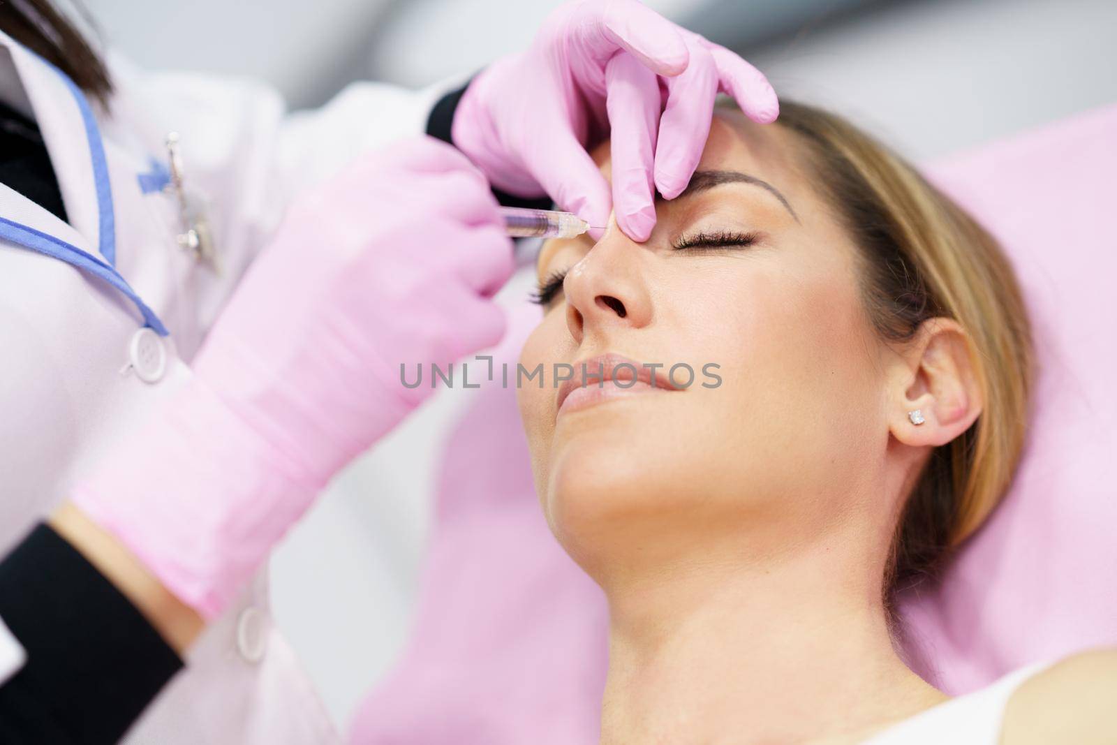 Doctor performing rhinoplasty by injection of hyaluronic acid in the nose of his patient, a middle-aged woman.