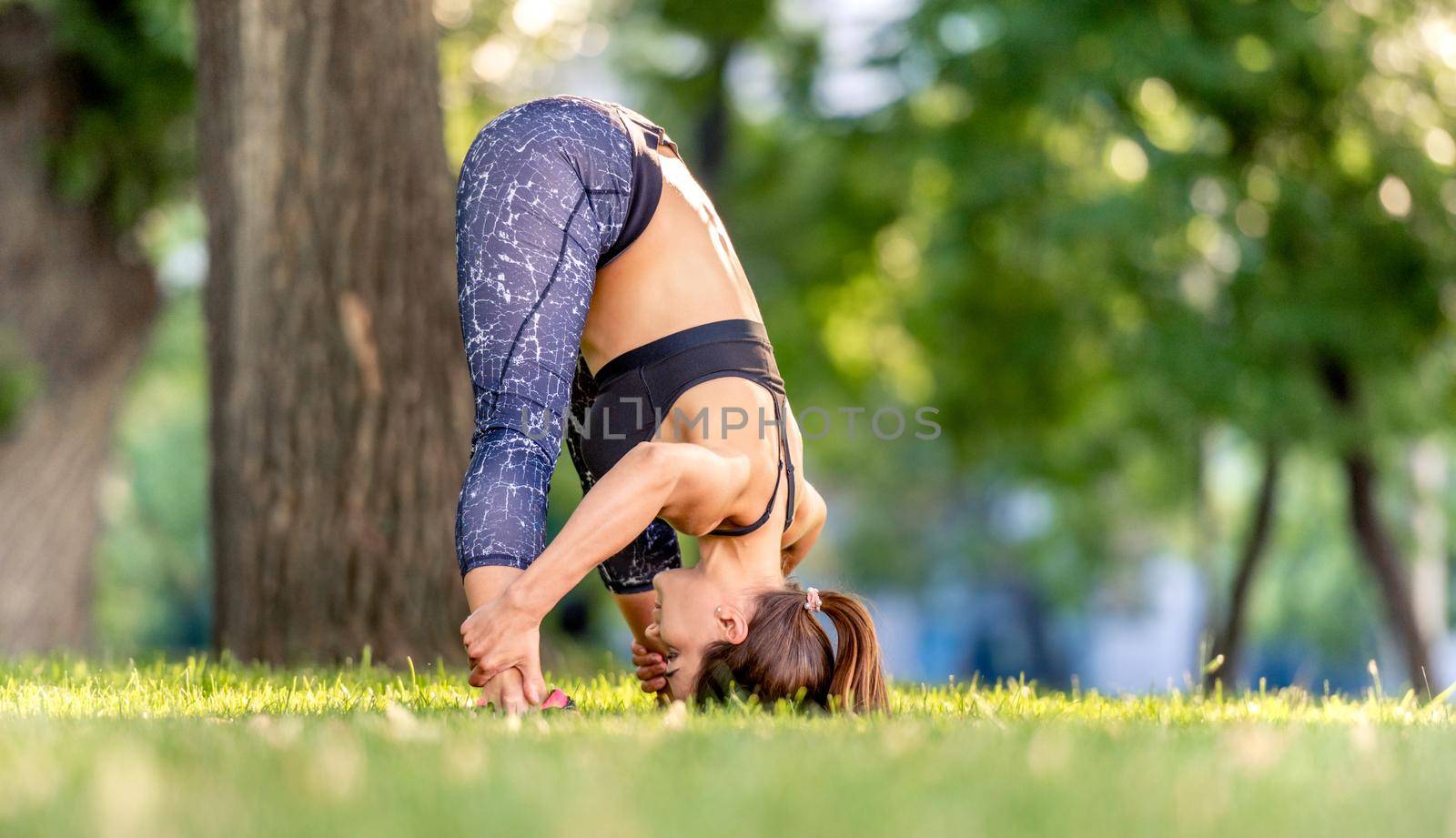 Beautiful girl doing yoga workout at nature and keeping her body down . Young woman exercising and stretching outdoors in the morning