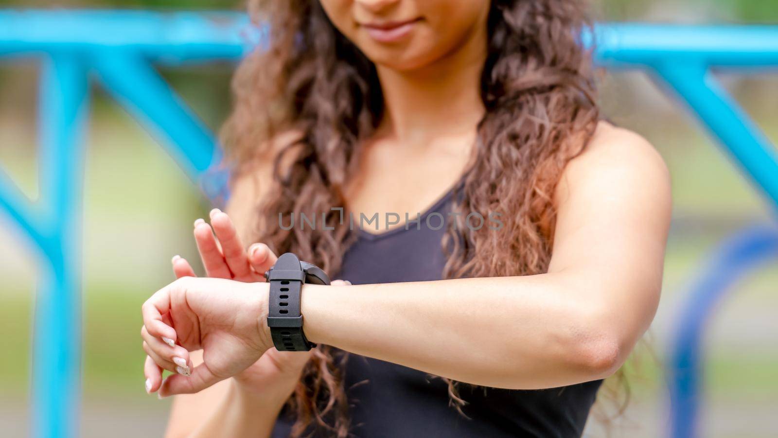 Sport girl looking at fitness tracker on her hand during workout outdoors. Athlete woman with watch bracelet at stadium