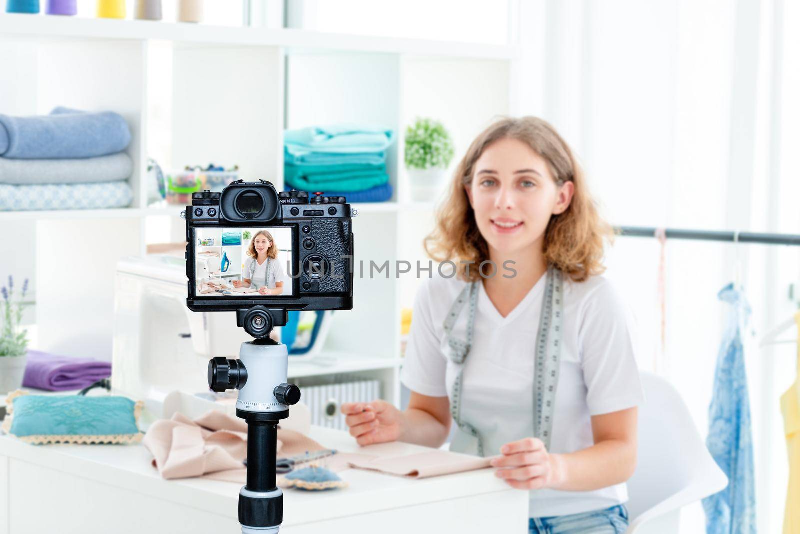 Smiling seamstress sitting at working desk with measuring tape. Blogger profession. Shooting with a camera for a blog