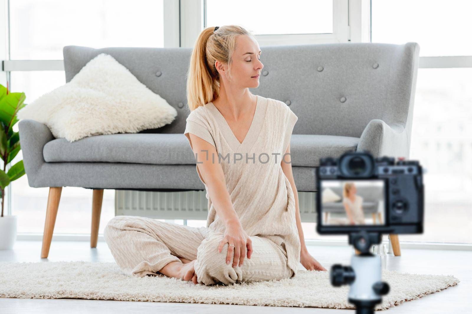 Blond girl turned to the side and stretch her back during morning yoga workout at home. Blogger profession. Shooting with a camera for a blog
