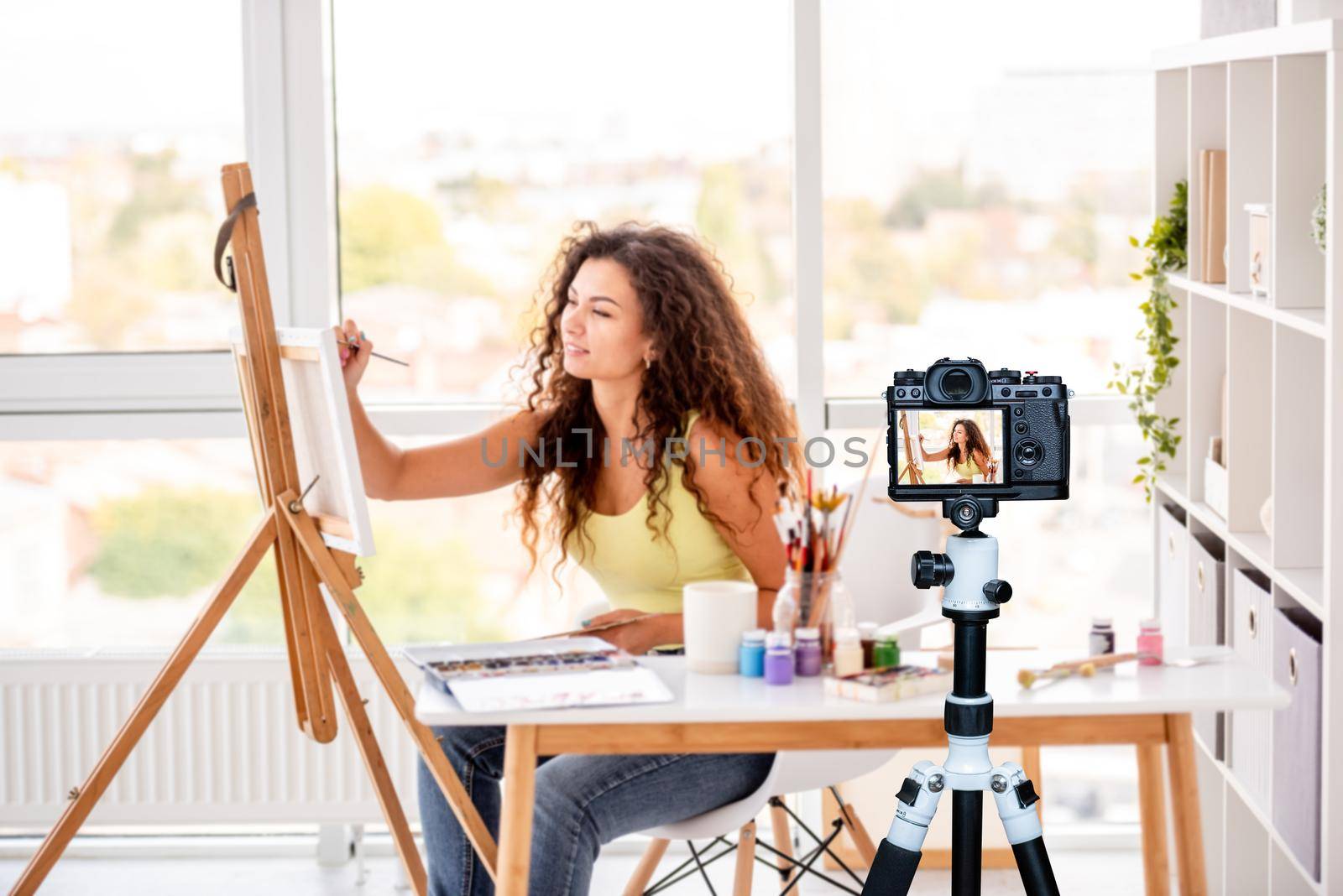 Cute girl painter making new picture sitting in workshop. Blogger profession. Shooting with a camera for a blog
