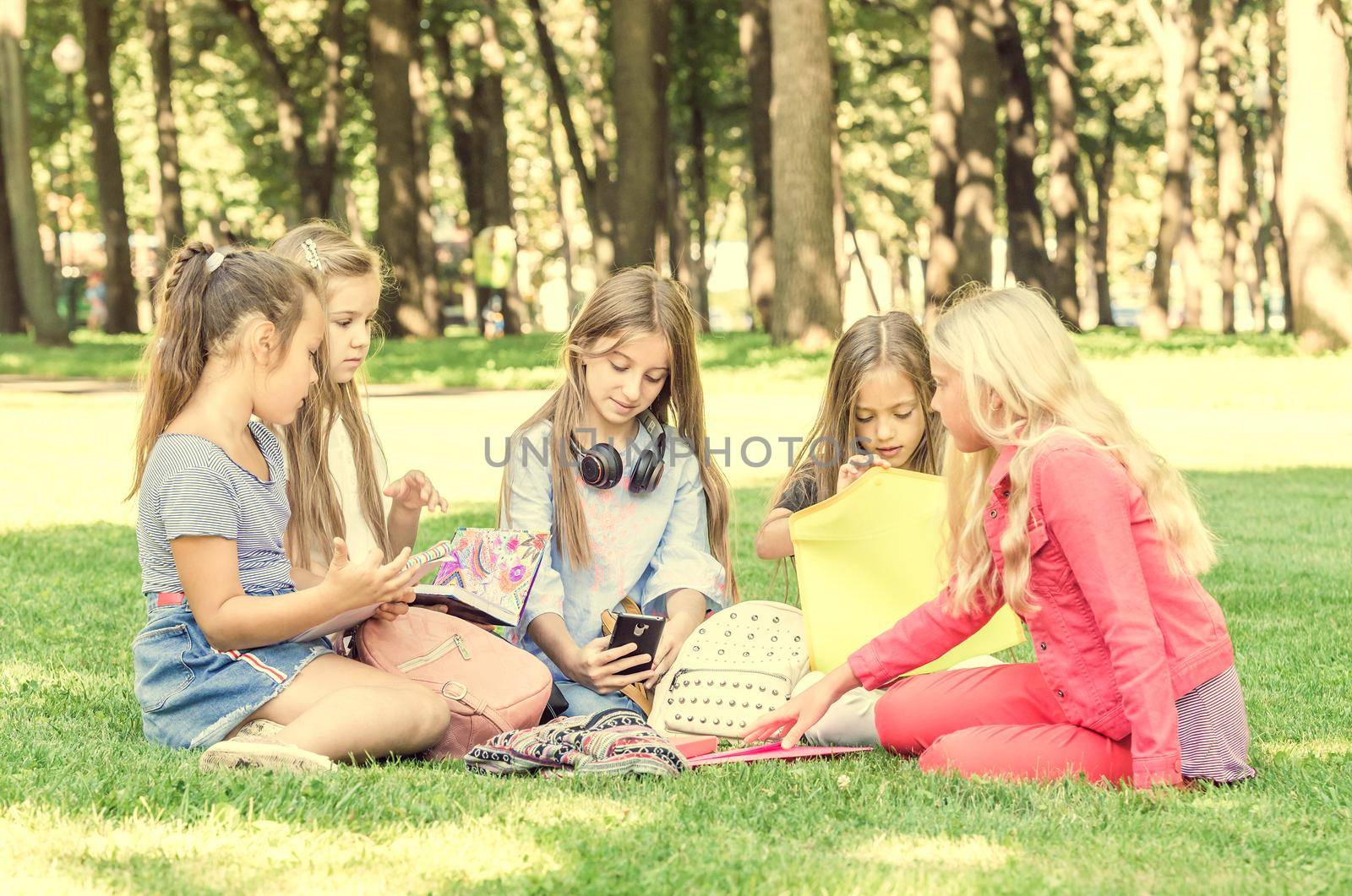 Friendly teens sitting with notebooks on the grass in the park