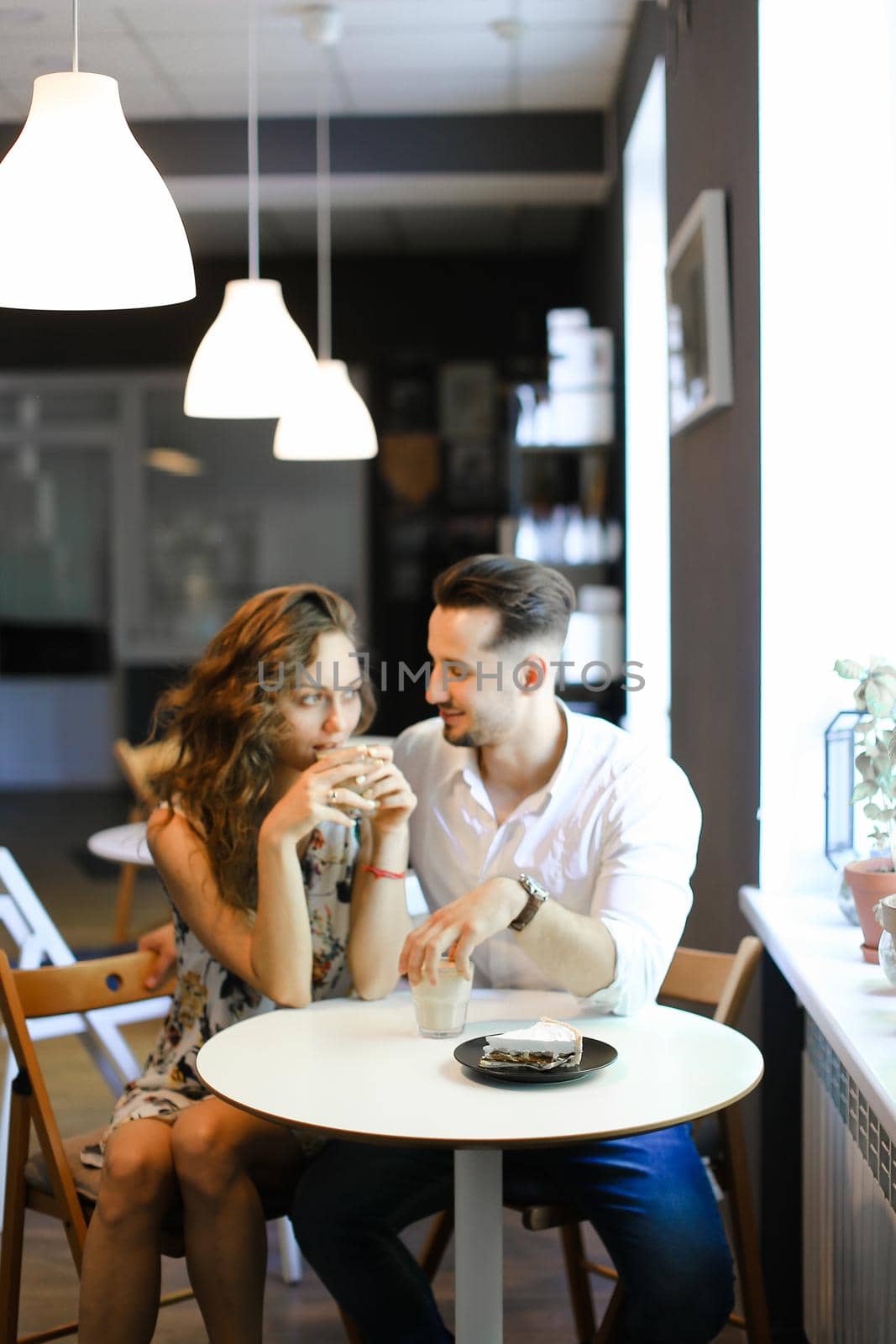 Young american husband hugging wife and sitting at cafe, drinking coffee. Concept of enjoing togetherness and having lunch.