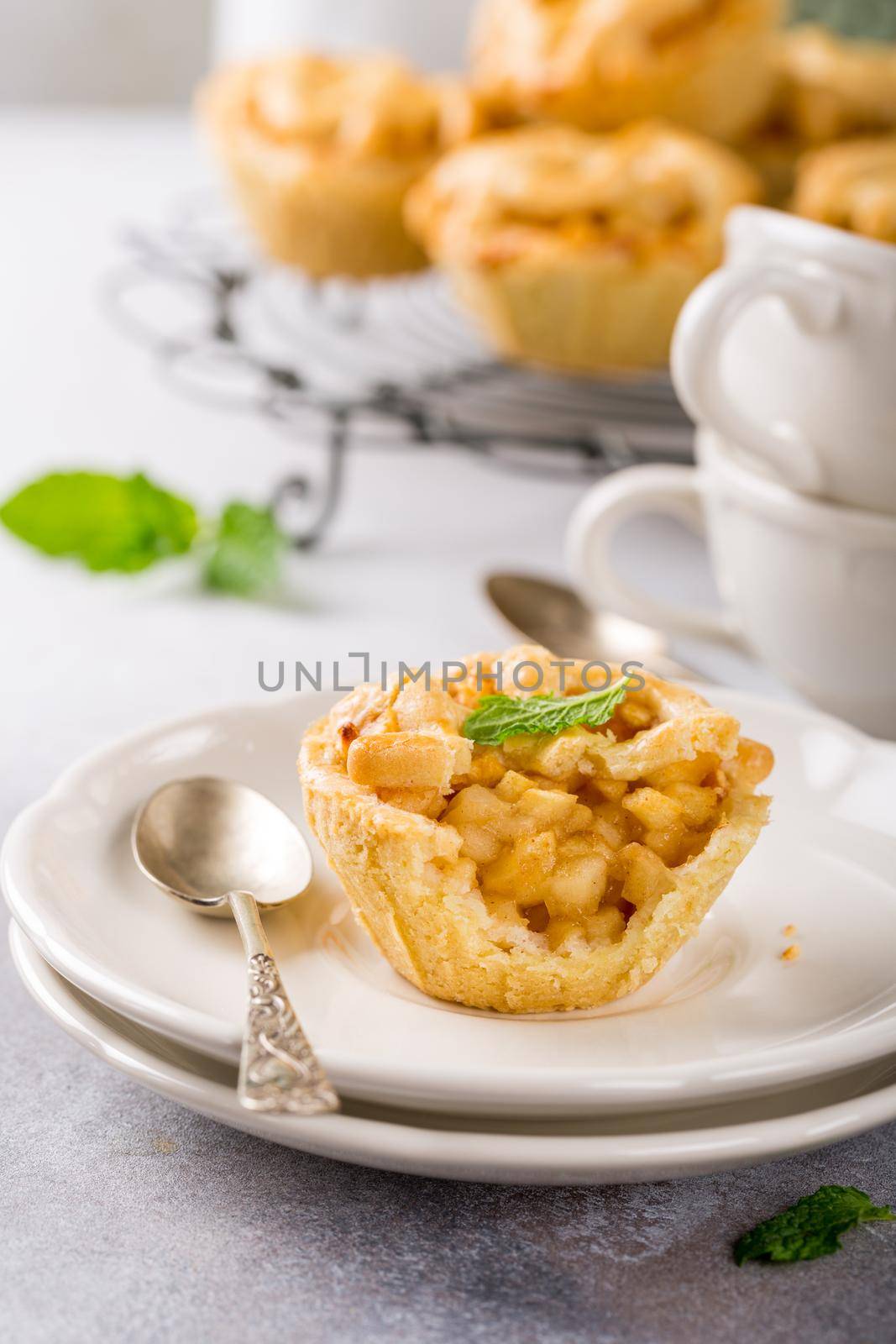 Homemade mini apple pies on white plates decorated with mint leaves on light concrete background. Healthy food concept.