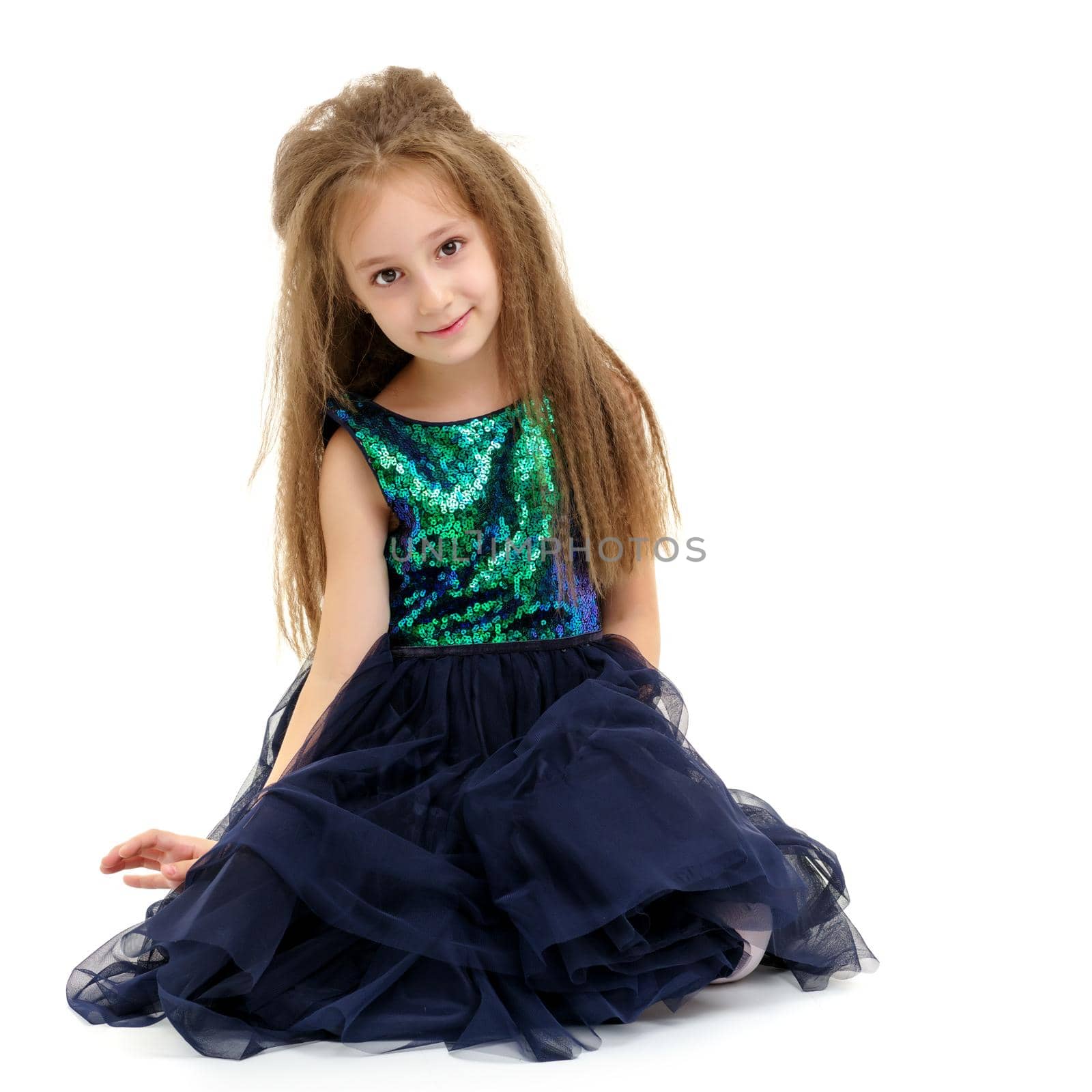 Beautiful little girl is sitting on the floor in the studio. The concept of a happy childhood, beauty and fashion. Isolated on white background.