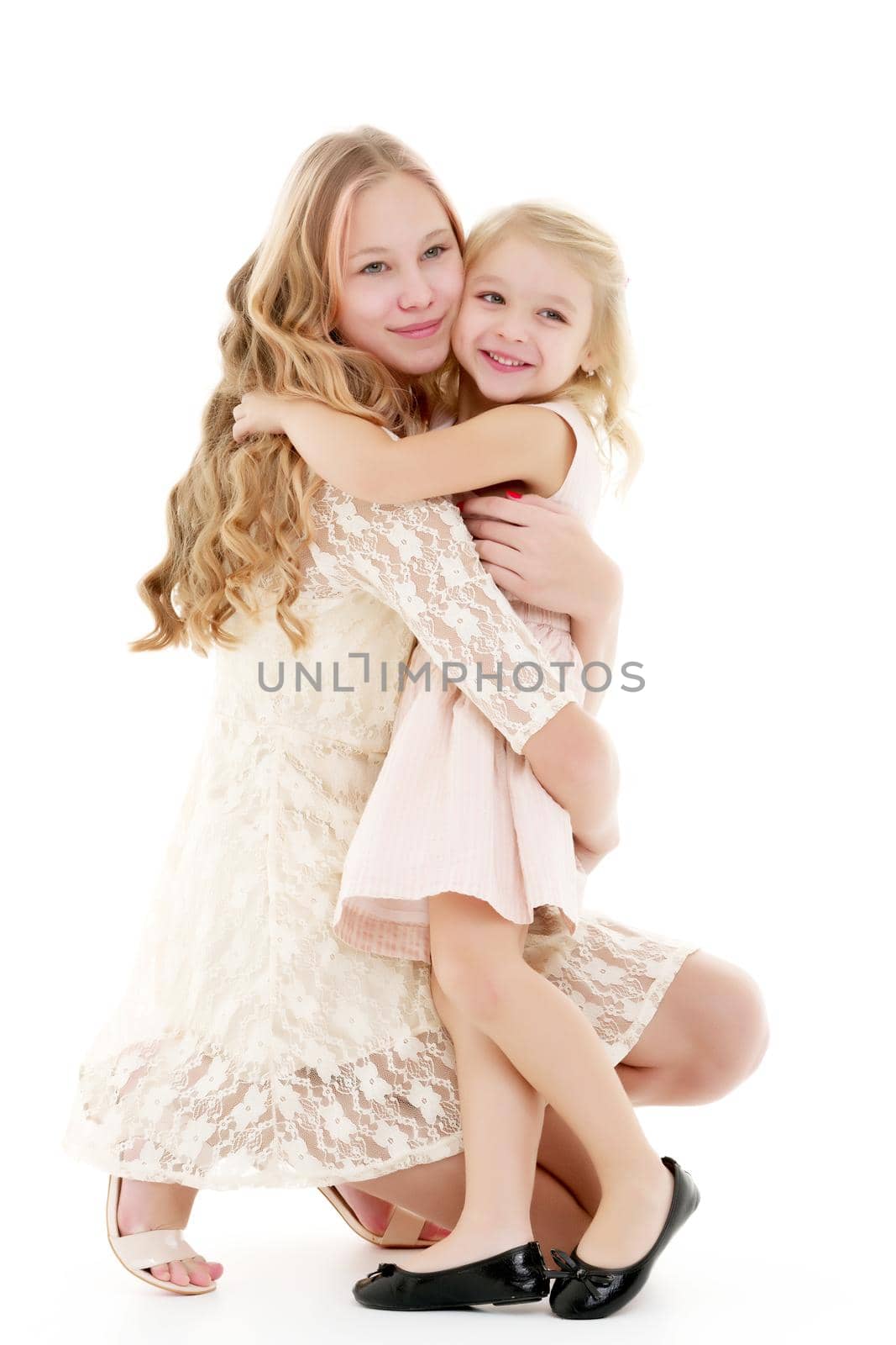 Beautiful young girl hugging her little sister. The concept of a happy childhood, family values. Isolated on white background.