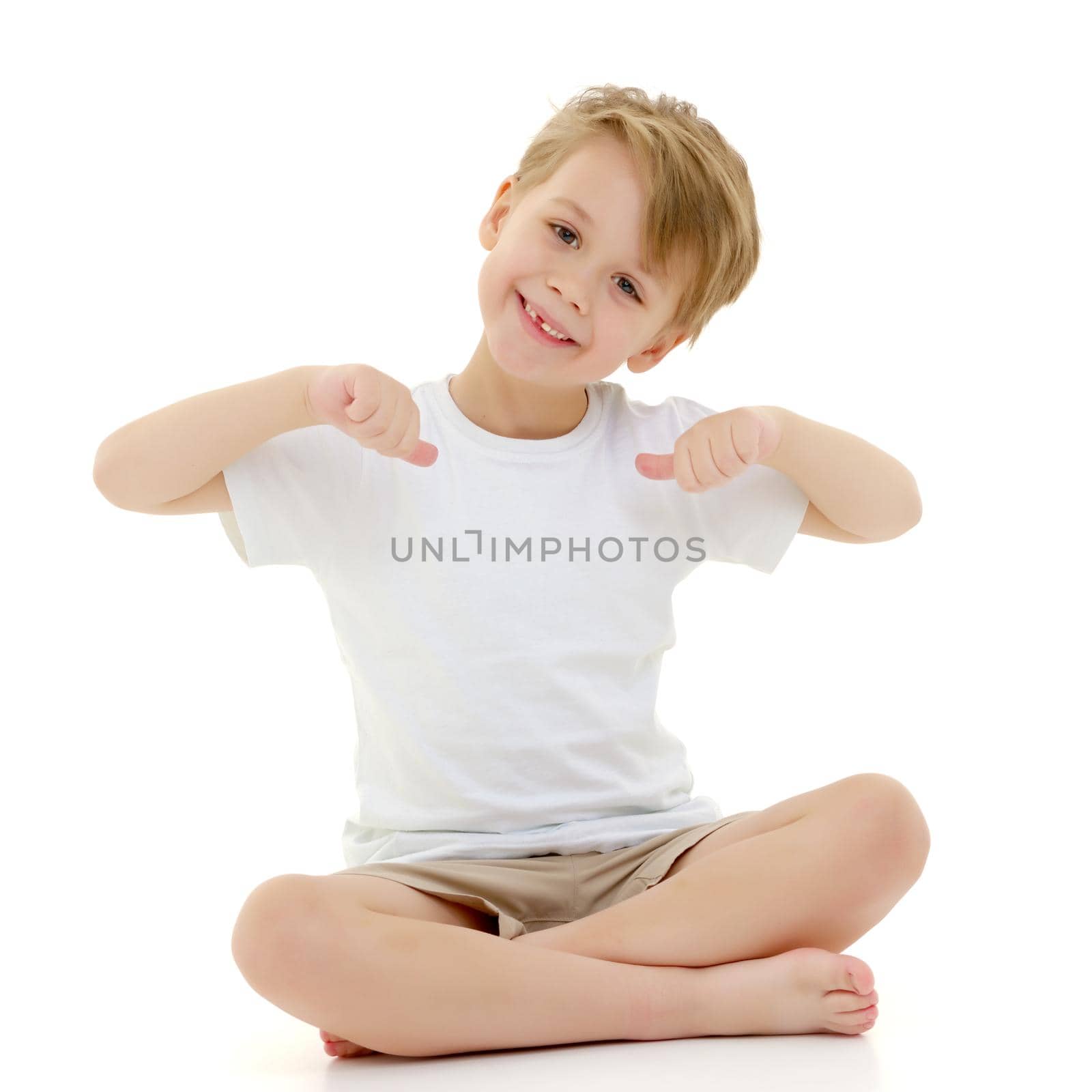 A cute little boy in a pure white T-shirt points his fingers at her. On a T-shirt, you can make an advertising inscription or picture. The concept of promoting children's products. Isolated on white background.