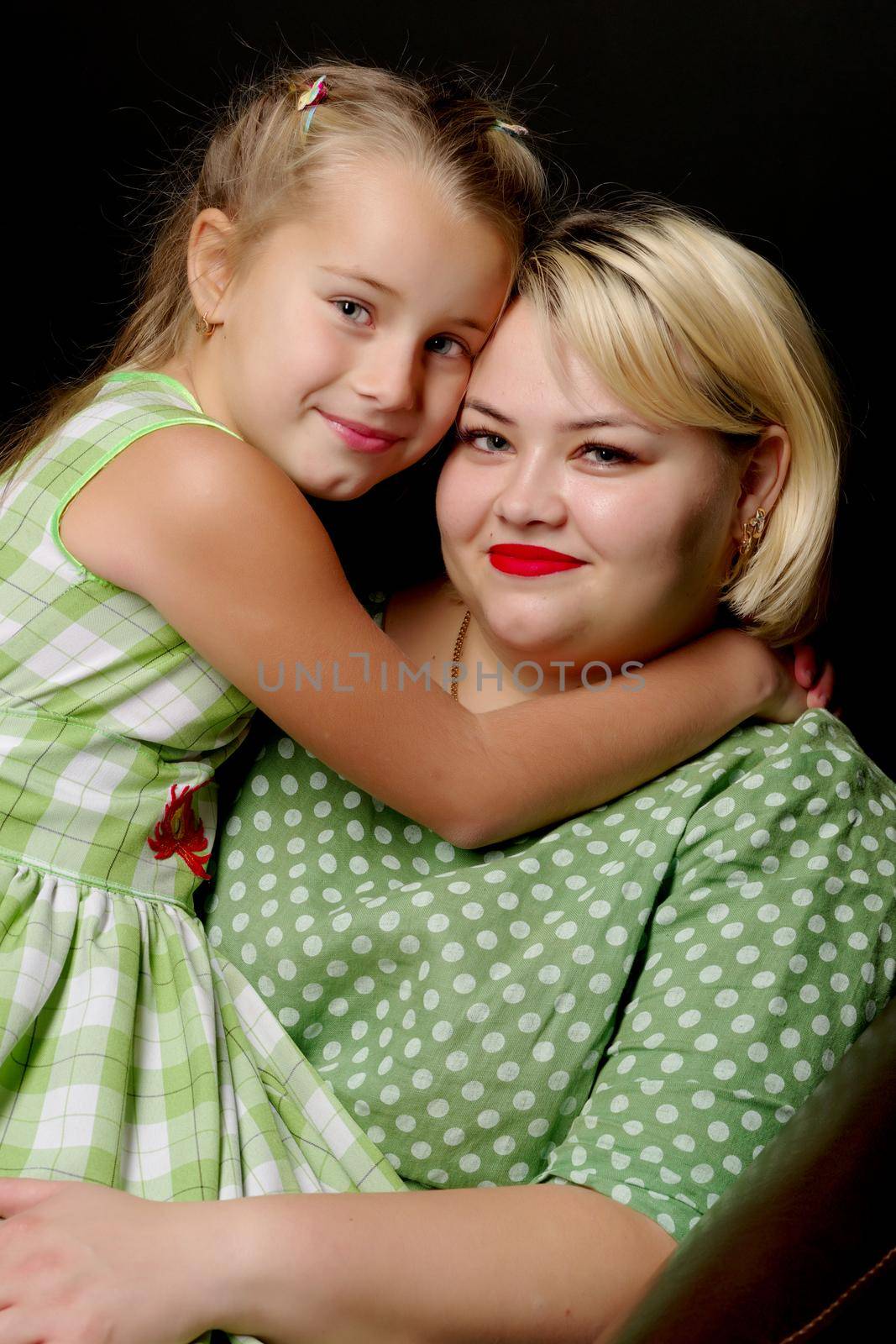 Happy family mom and daughter are hugging on a black background in the studio.