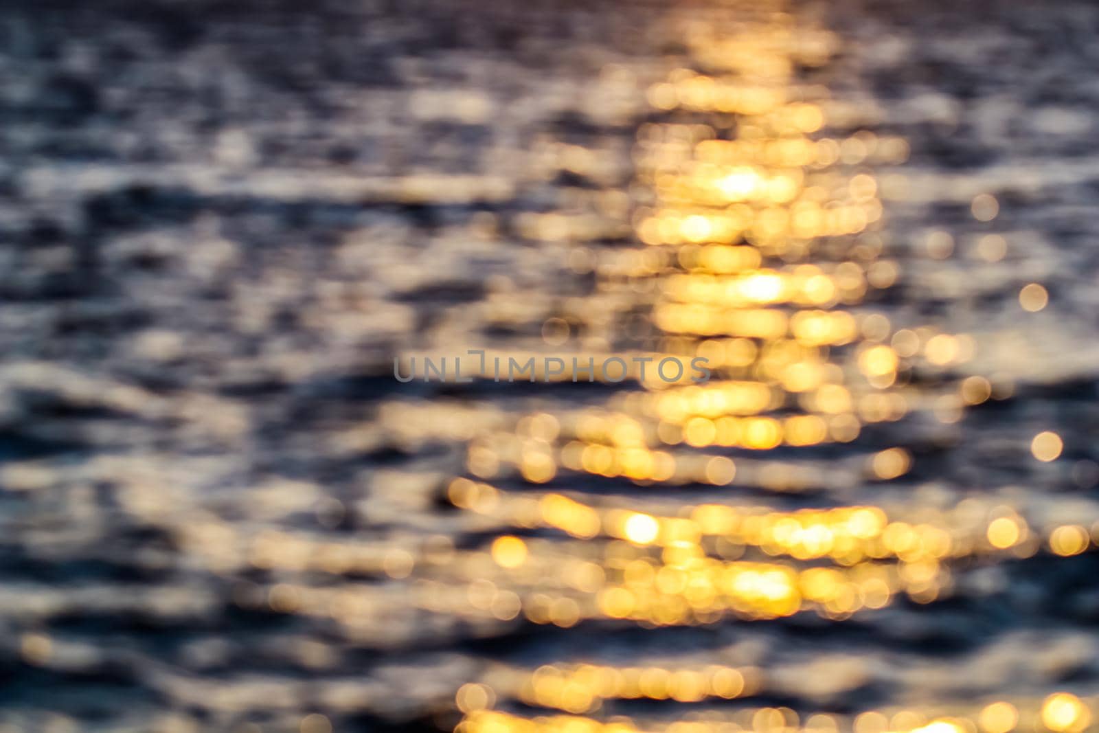 Blurred texture background for design. Golden bokeh of sea waves at sunset. Summer vacation and coastal nature concept