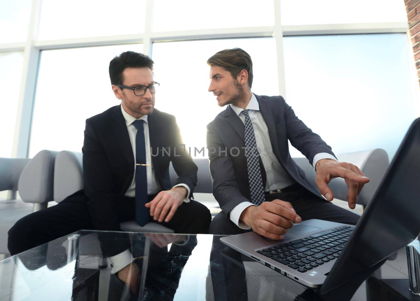 two businessmen discussing information from a laptop by asdf