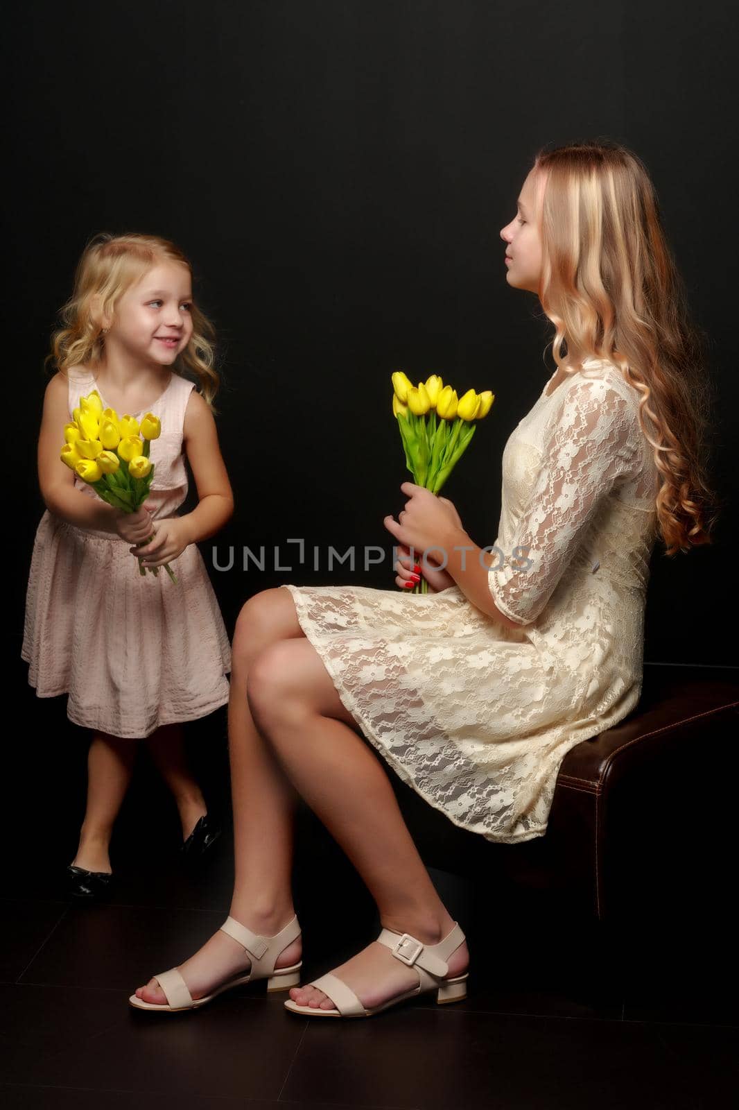 Two beautiful little girls with flowers in the studio. The concept of happy people, children.