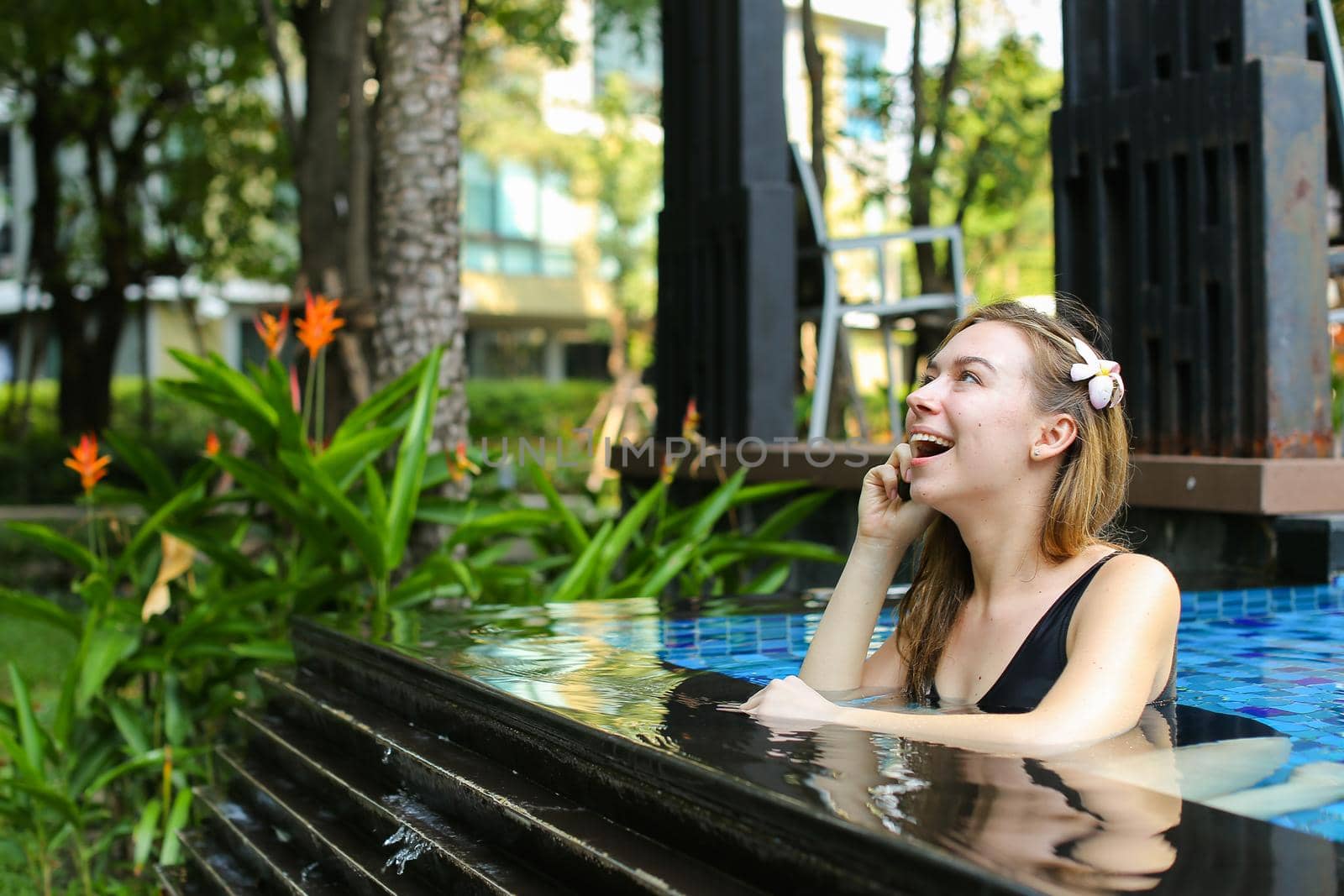 sunshine portrait of happy beautiful woman talking on smart phone swimming at pool. concept of international calls, travel and resting time