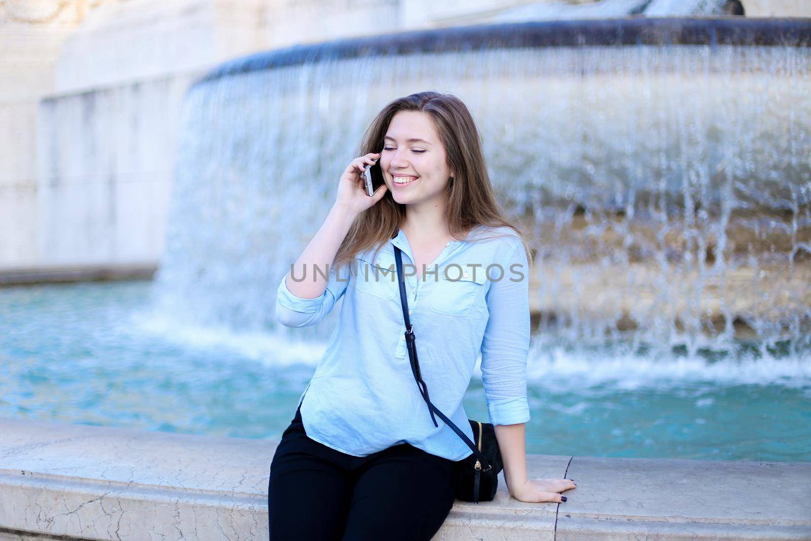 Young businesswoman speaking by smartphone in Trevi fountain background. Concept of modern technology, advantageous tariff plan and summer vacations in Europe.