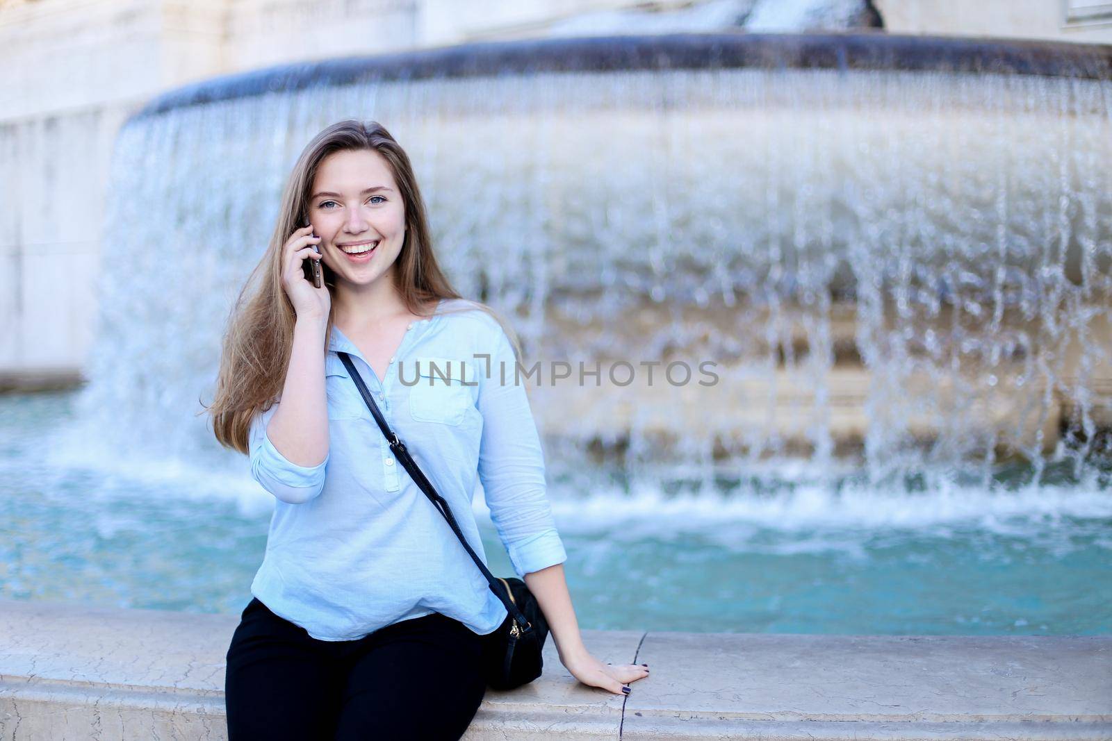 Young woman talking by smartphone in Trevi fountain background. Concept of modern technology, advantageous tariff plan and summer vacations in Europe.