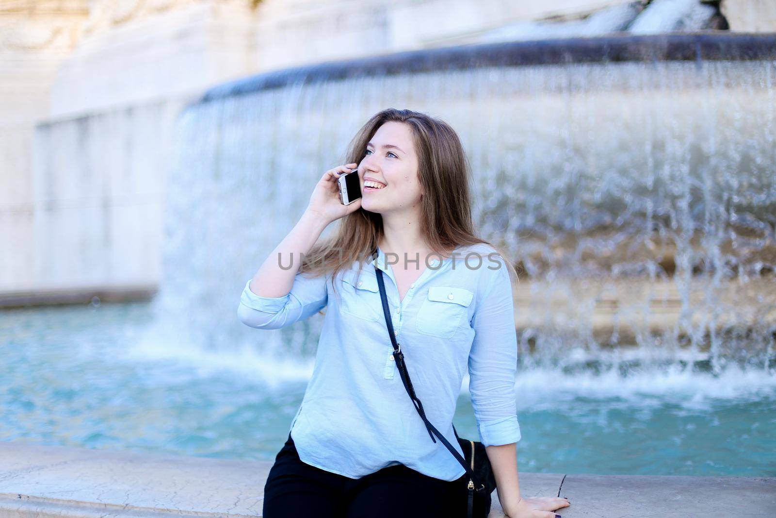 Young girl speaking by smartphone in Trevi fountain background. Concept of modern technology, advantageous tariff plan and summer vacations in Europe.