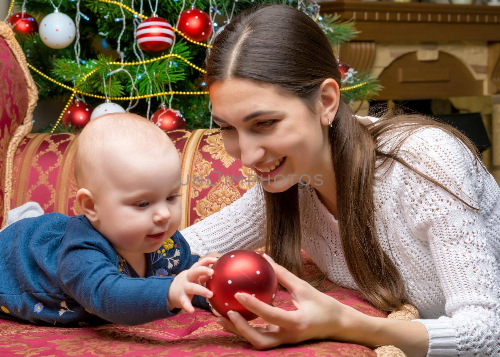 Happy young mother with her little daughter, on Christmas Eve near the Christmas tree with gifts and toys. The concept of holidays and happy childhood.