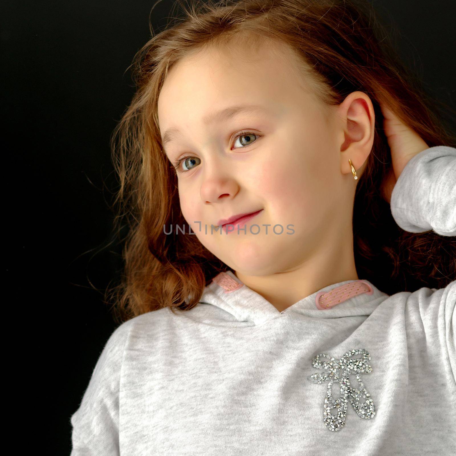 A beautiful little girl straightens her hair on her head. The concept of beauty and fashion, photo on the cover of the magazine.Studio portrait on black background.