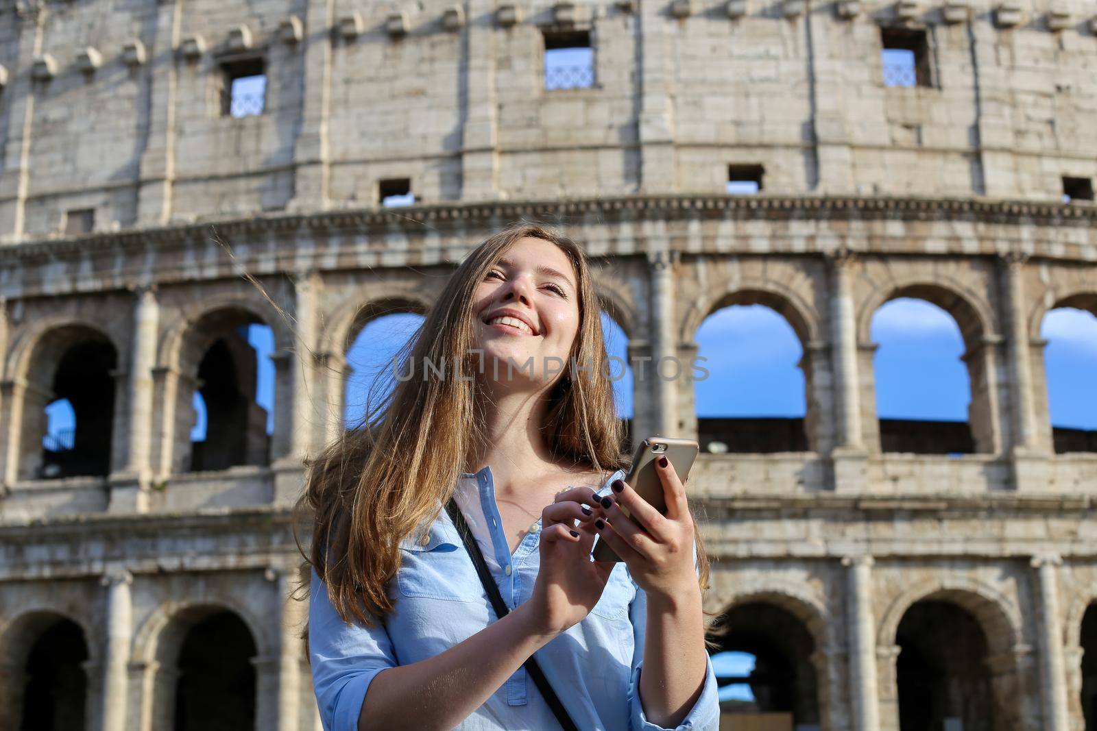 Young girl surfing by smartphone in Colosseum background in Rome. Concept of last minute tours to Italy and using Internet by modern gadget.