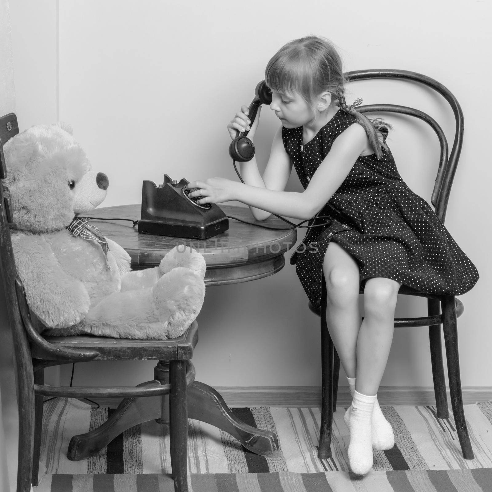 A sweet little girl is ringing on the old phone. The concept of a happy childhood, retro style, old things of the fifties of last century.