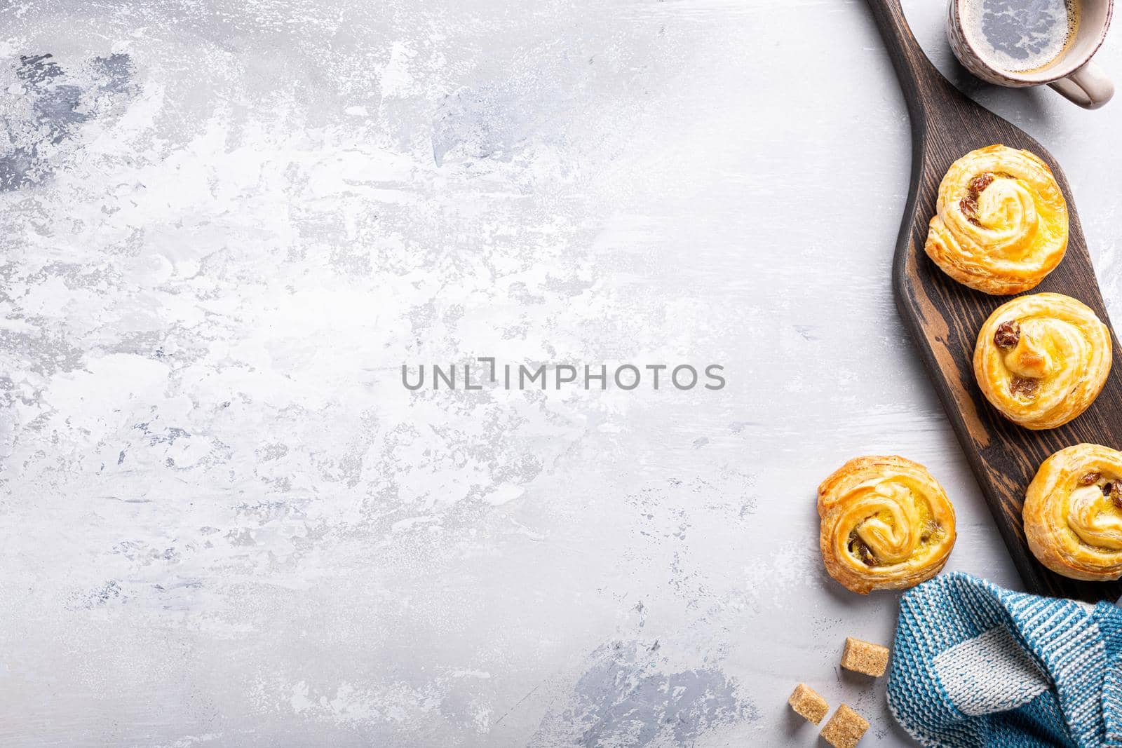 Food background with fresh pastry sweet swirl buns with raisins on wooden board for breakfast or brunch and coffee. Top view, copy space.